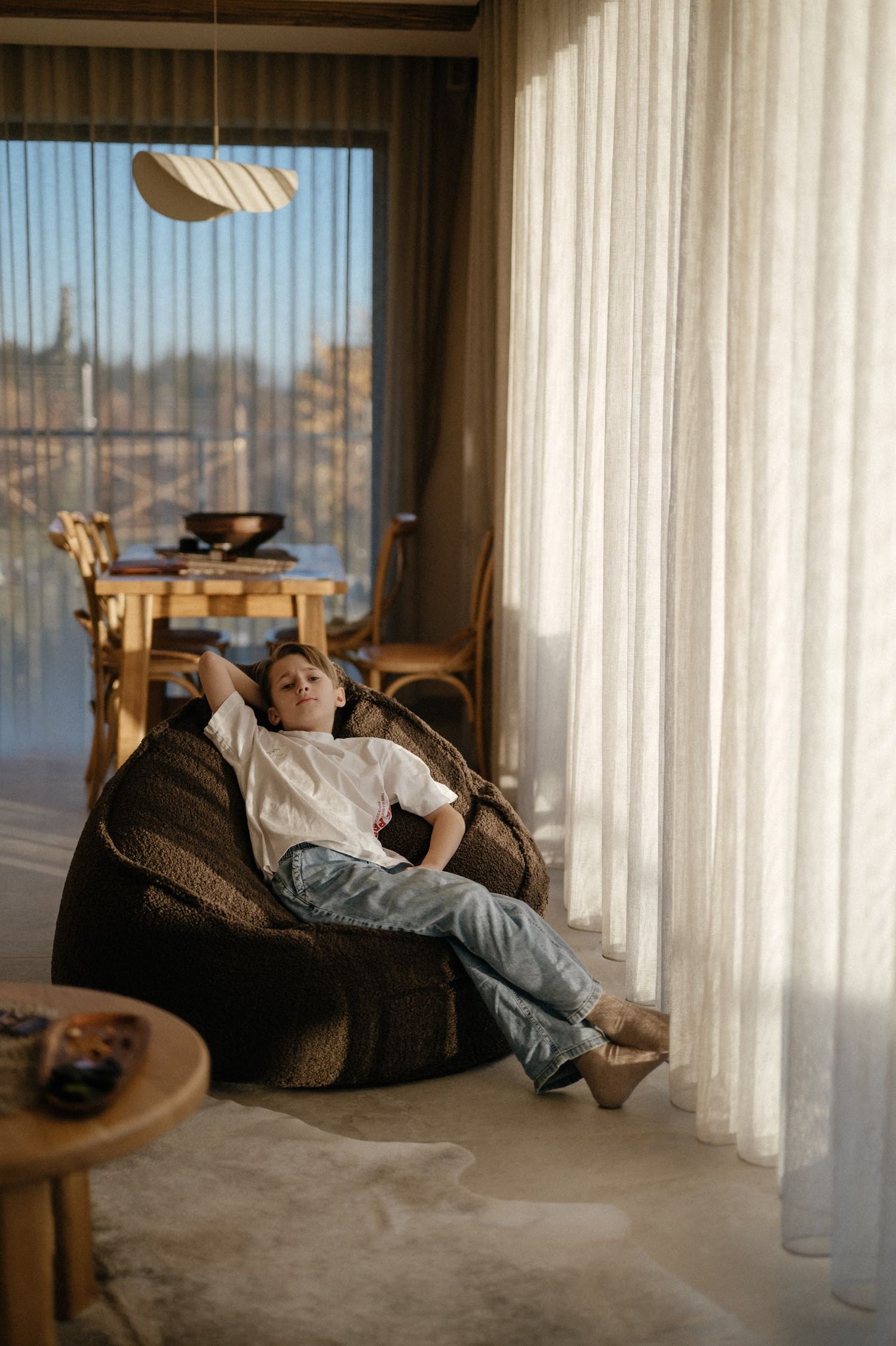 Young man relaxing in a wicker chair by sheer curtains in a modern living room with scenic views.