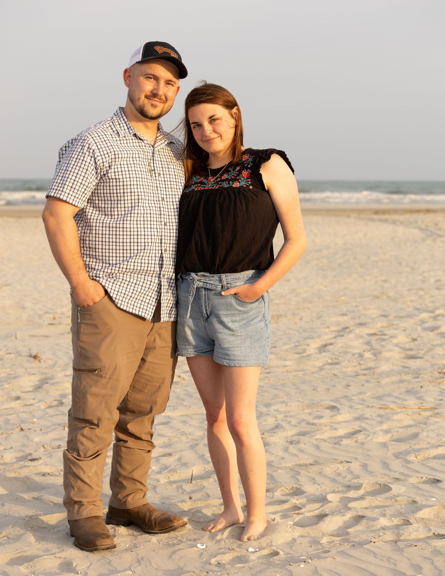 Smiling couple posing together on sandy beach at golden hour near ocean shoreline.
