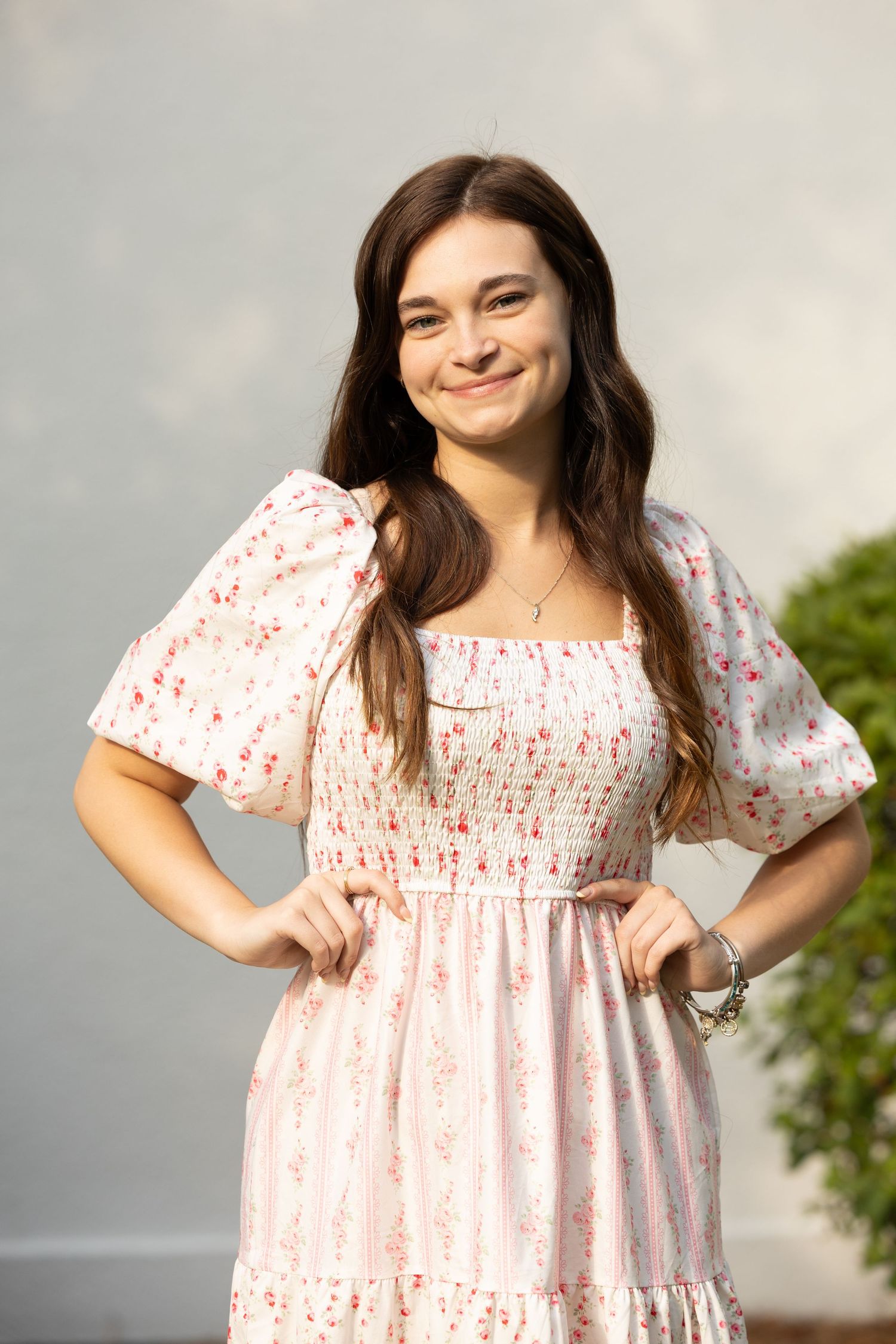 Smiling young woman in pink floral midi dress posing confidently with hands on hips.