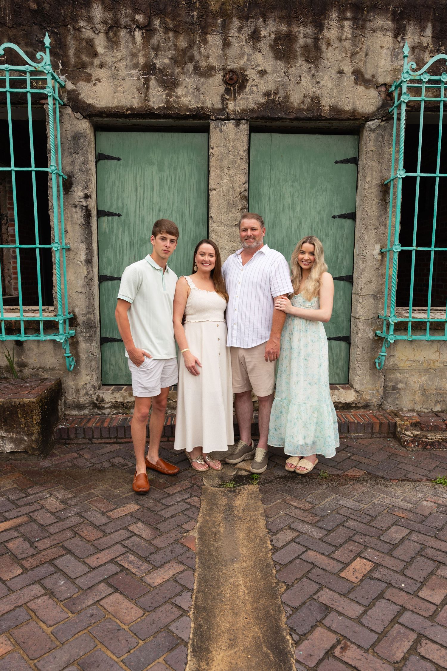 Family of four posing in front of vintage green doors on a cobblestone street.