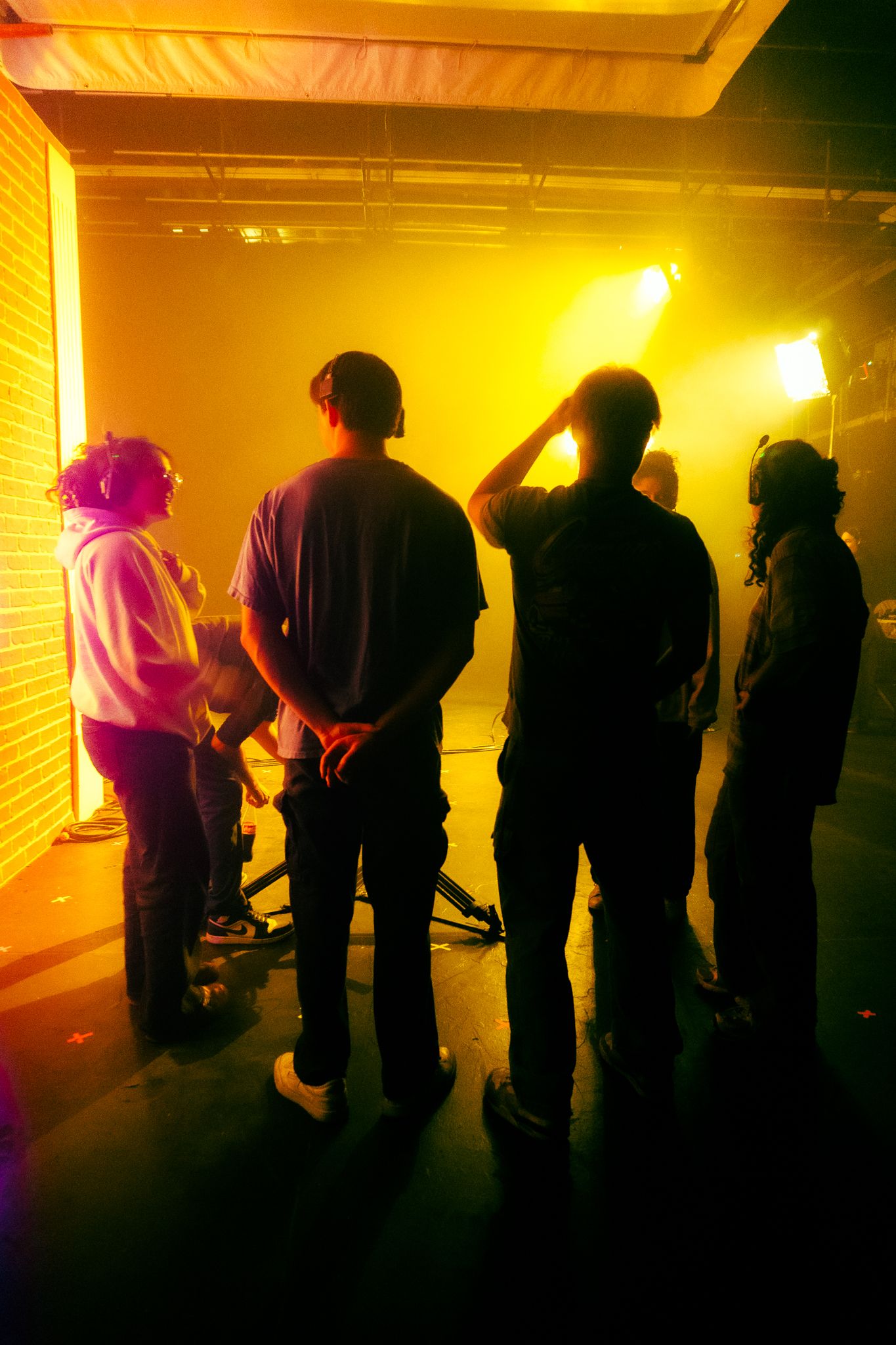 Four crew members stand silhouetted against intense yellow fog lights on a professional film studio set.