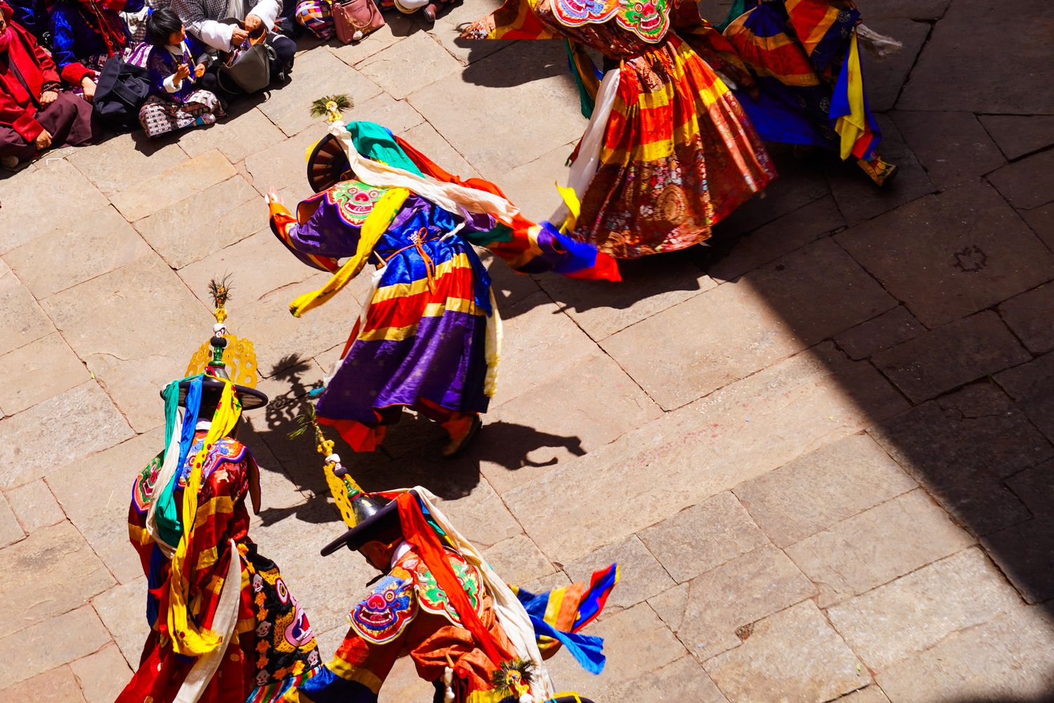Masked dancers in vibrant traditional costumes perform at a Bhutanese Tsechu religious festival.