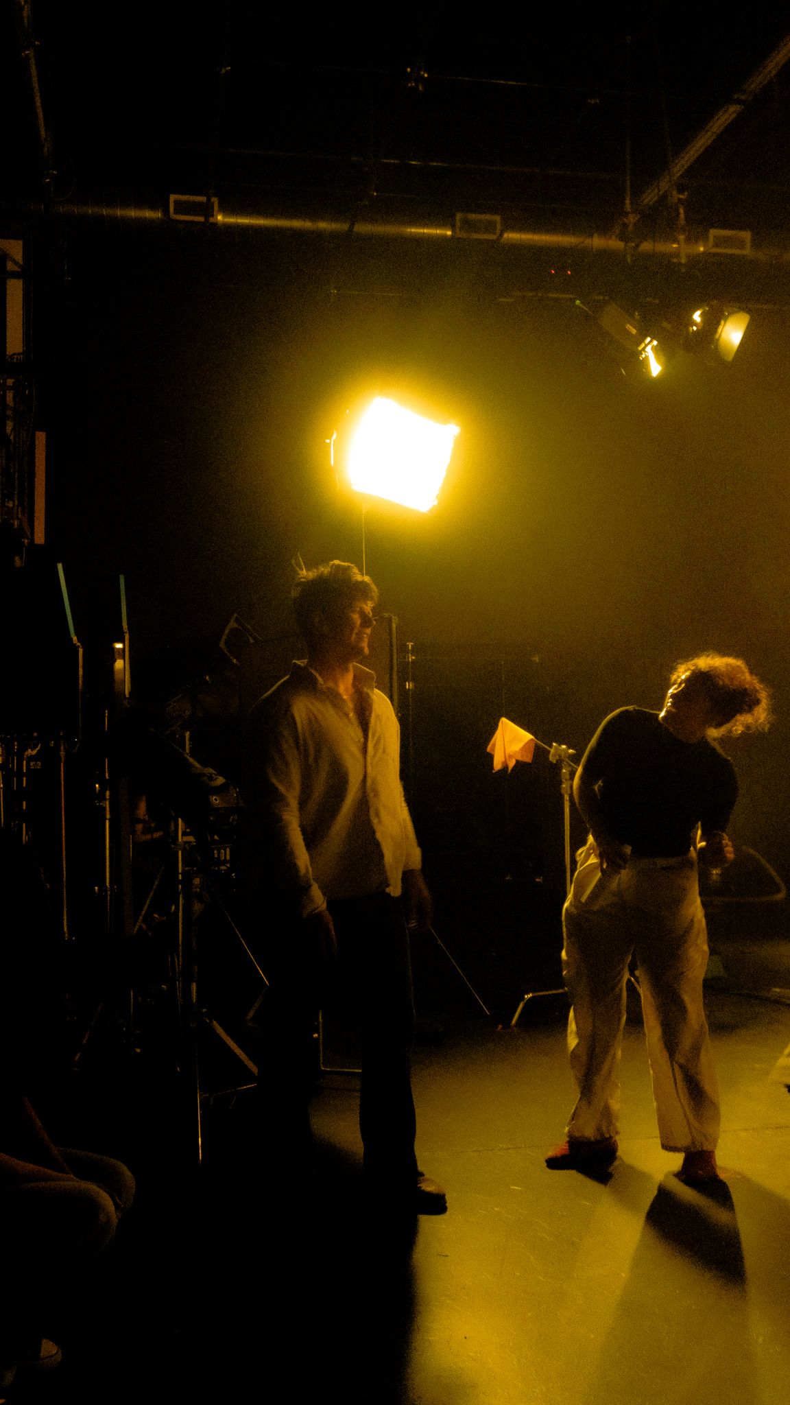 Two people reviewing script under bright studio light on dark film set.