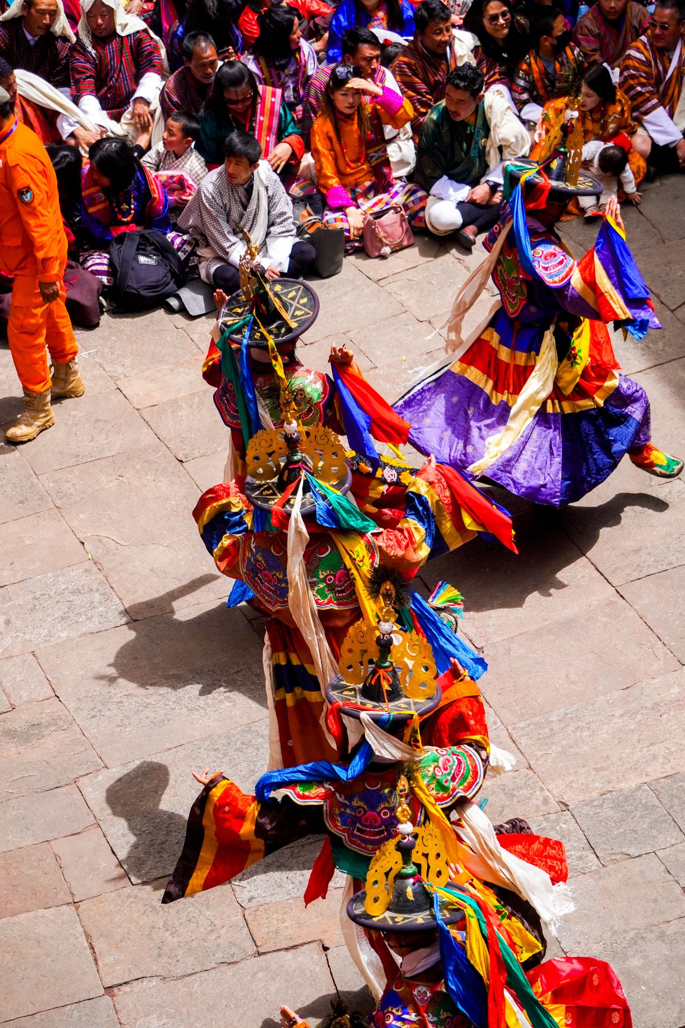 Overhead view of elaborately costumed Tibetan Cham dancers performing before seated spectators at festival.
