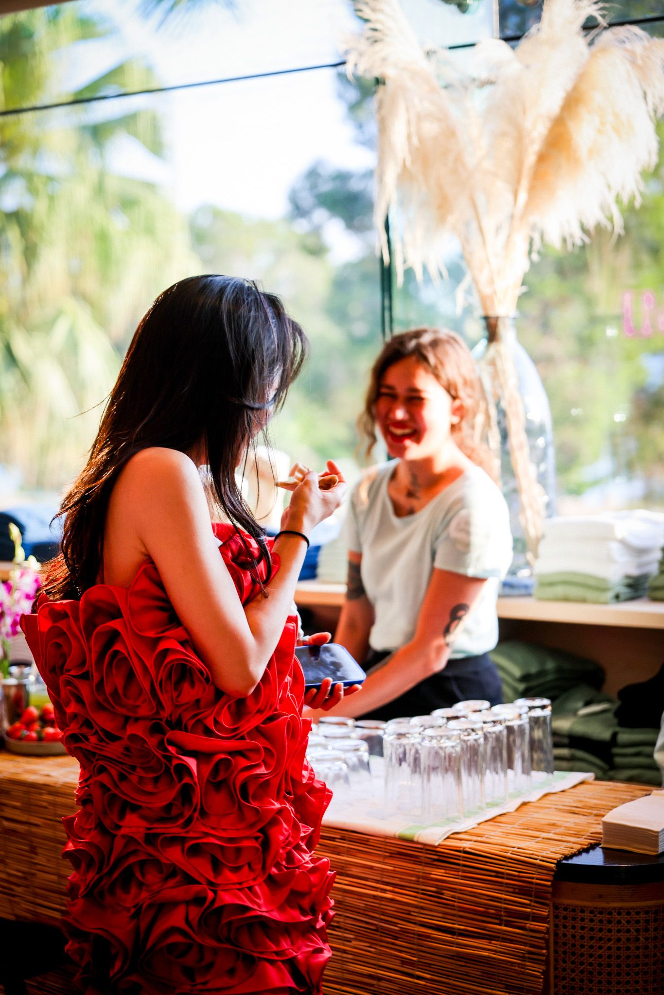 Woman in red ruffled dress at a bar counter speaking with a smiling bartender in white.