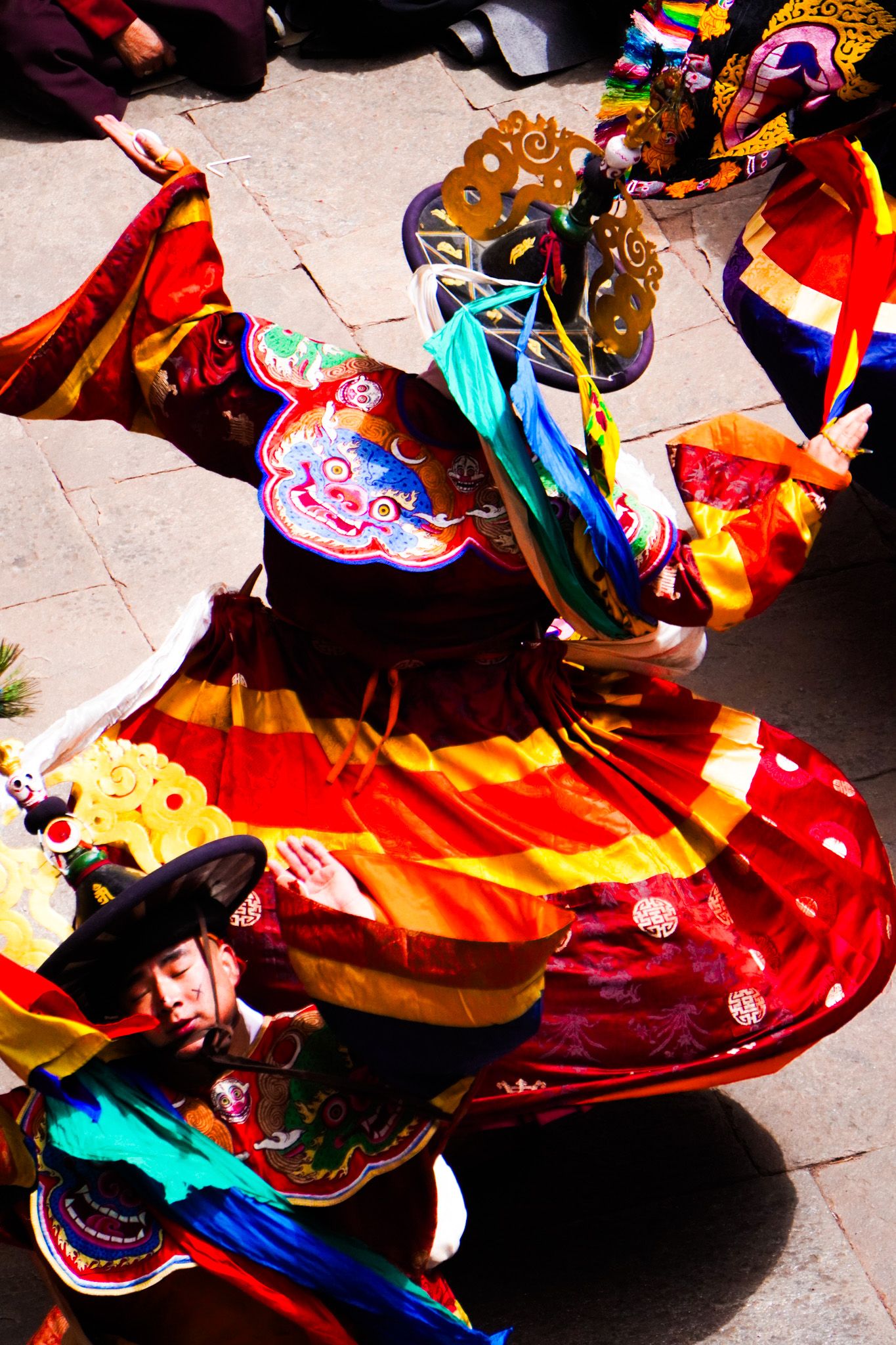 Aerial close-up of Bhutanese Cham dancer in vivid red and gold ceremonial robes performing traditional sacred Tsechu festival dance.