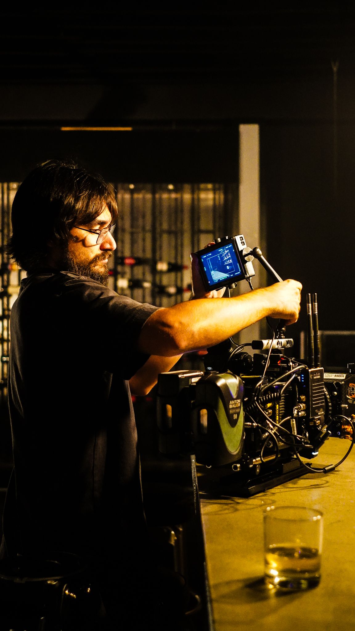 Cinematographer adjusting a professional cinema camera on a bar counter in a dimly lit studio.