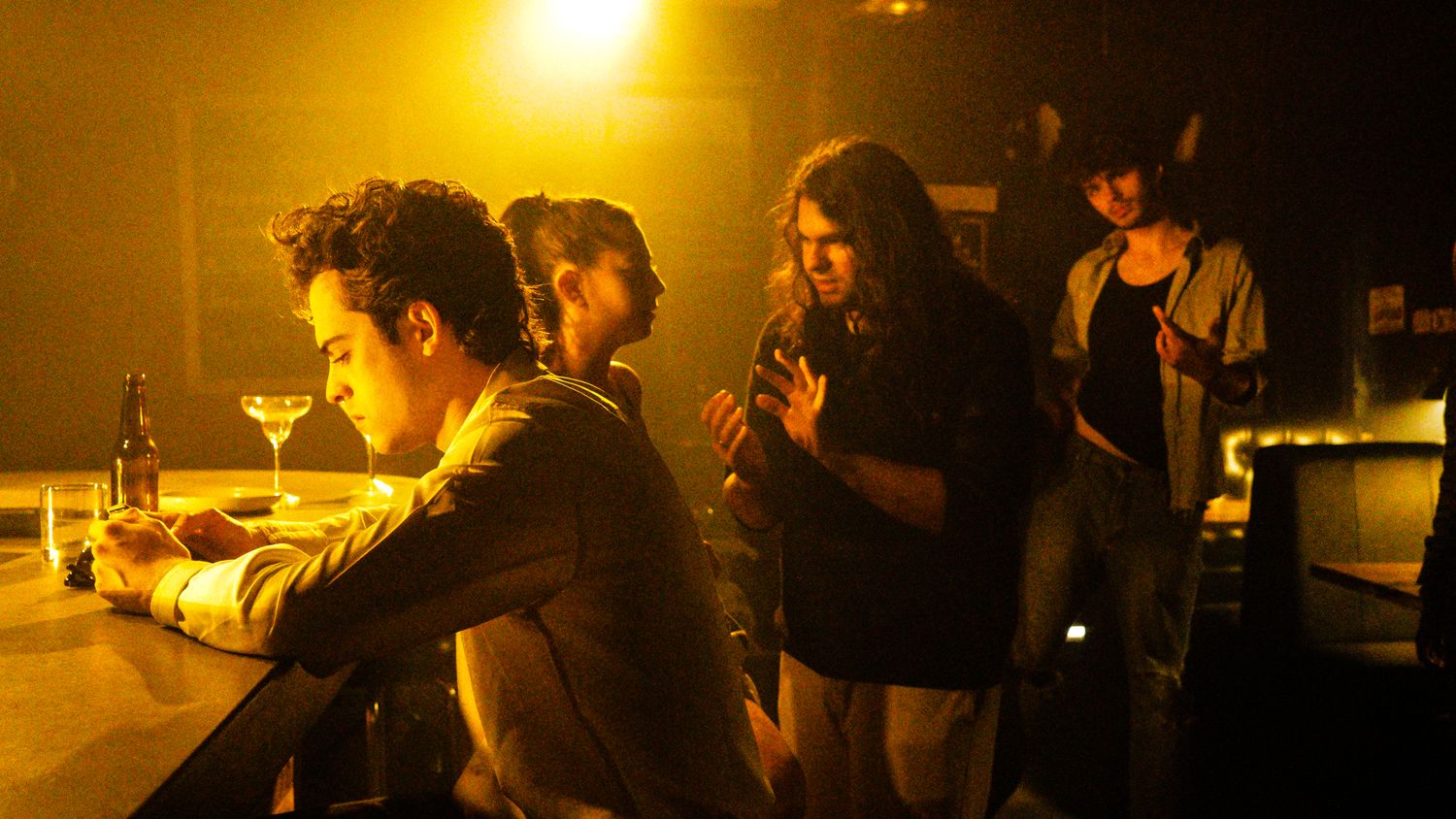 Group of people socializing at a dimly lit bar counter with warm amber lighting and drinks.