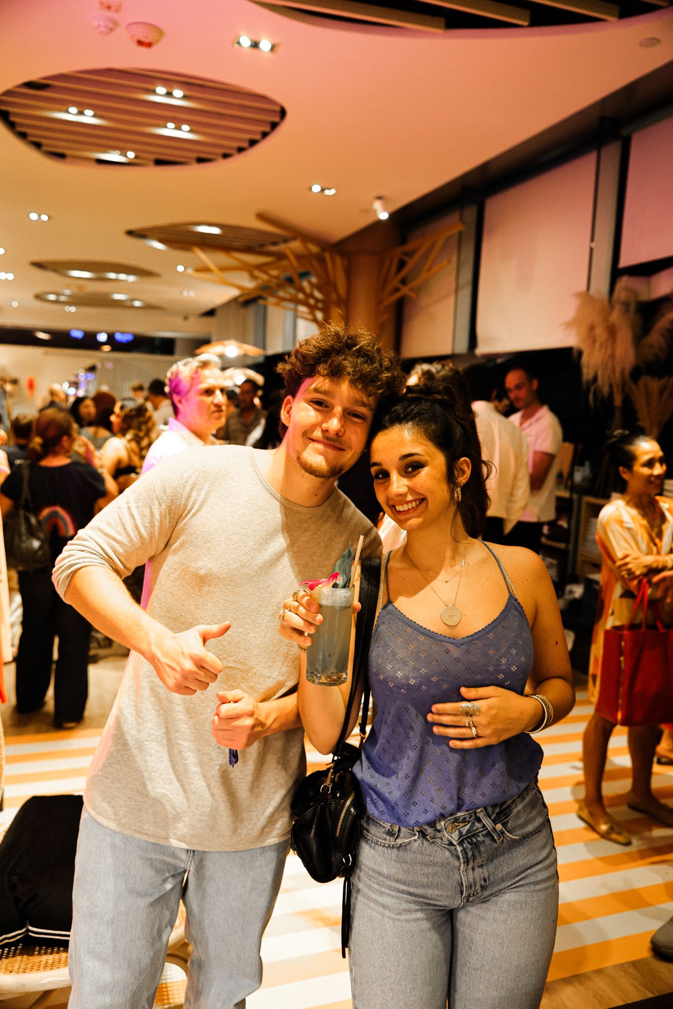 A young couple smiles for a photo at a casual indoor social gathering, man holding a cocktail.