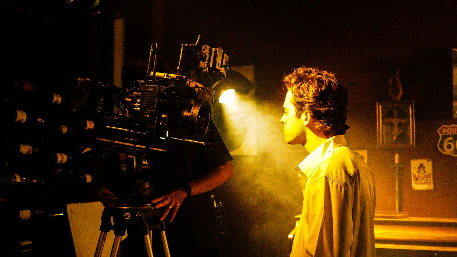 Person standing beside large professional film camera in smoky bar setting.
