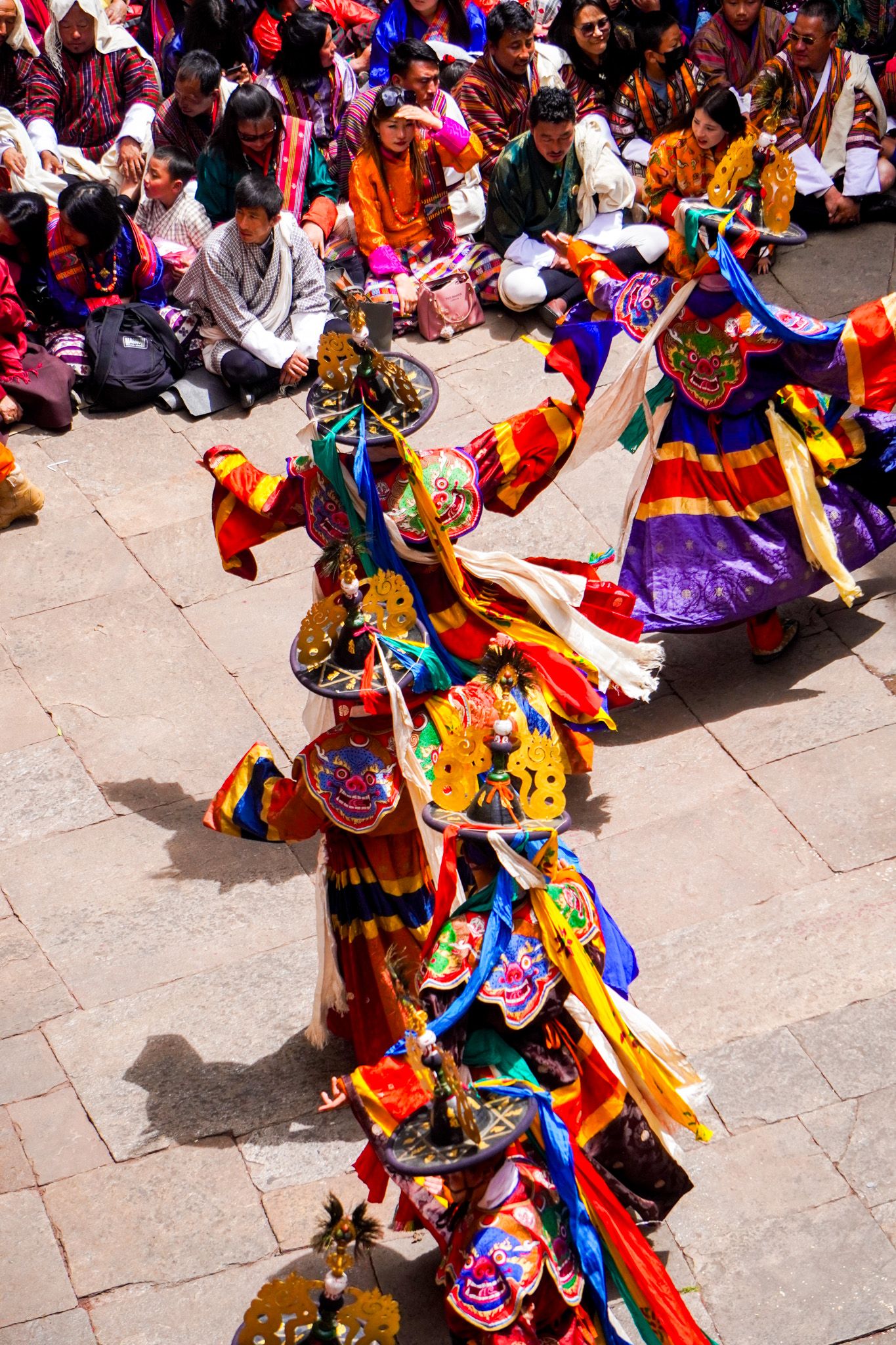 Aerial view of masked Tibetan Cham dancers in colorful robes performing traditional Buddhist ritual dance.