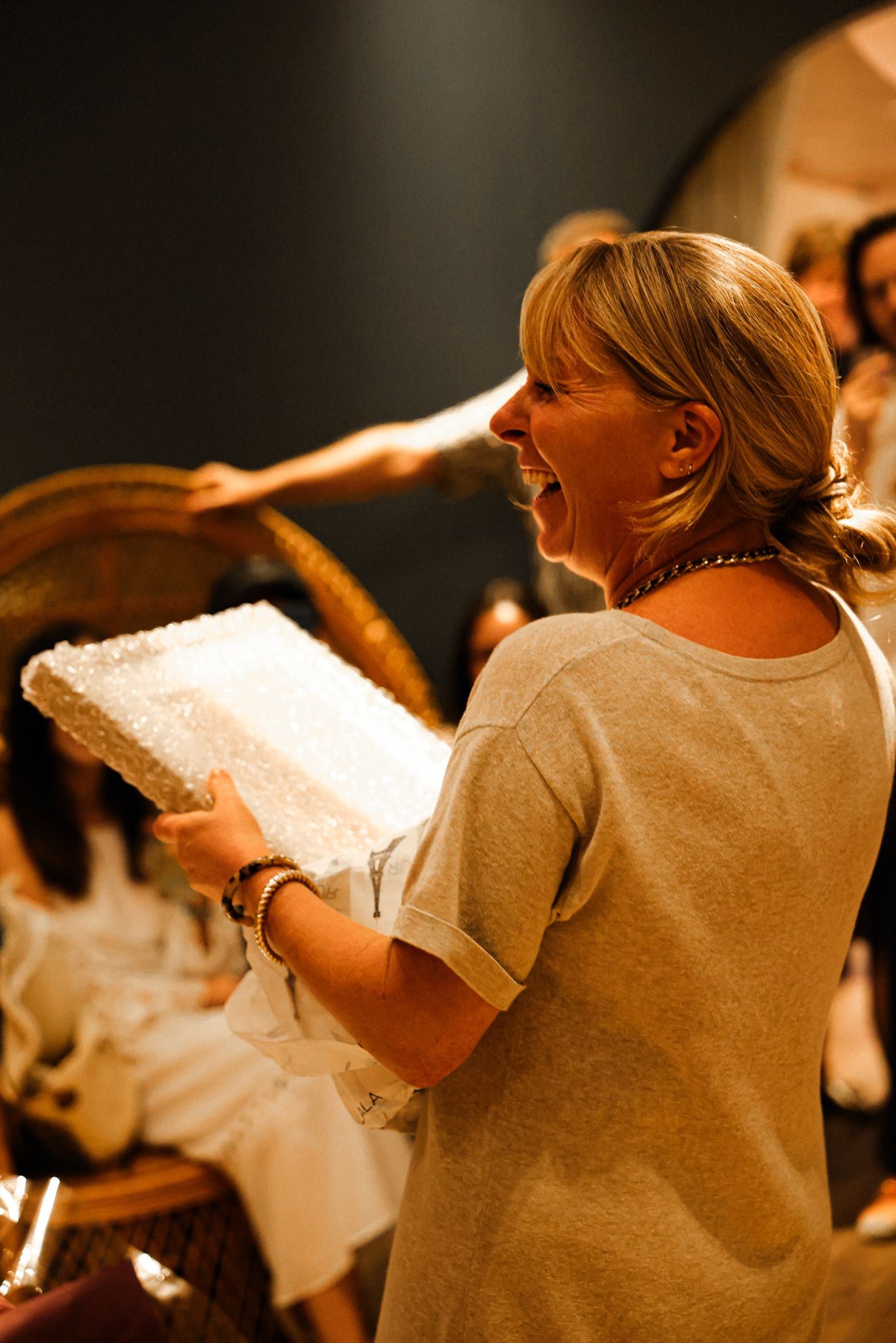 An excited blonde woman holds a white textured book at an indoor event.