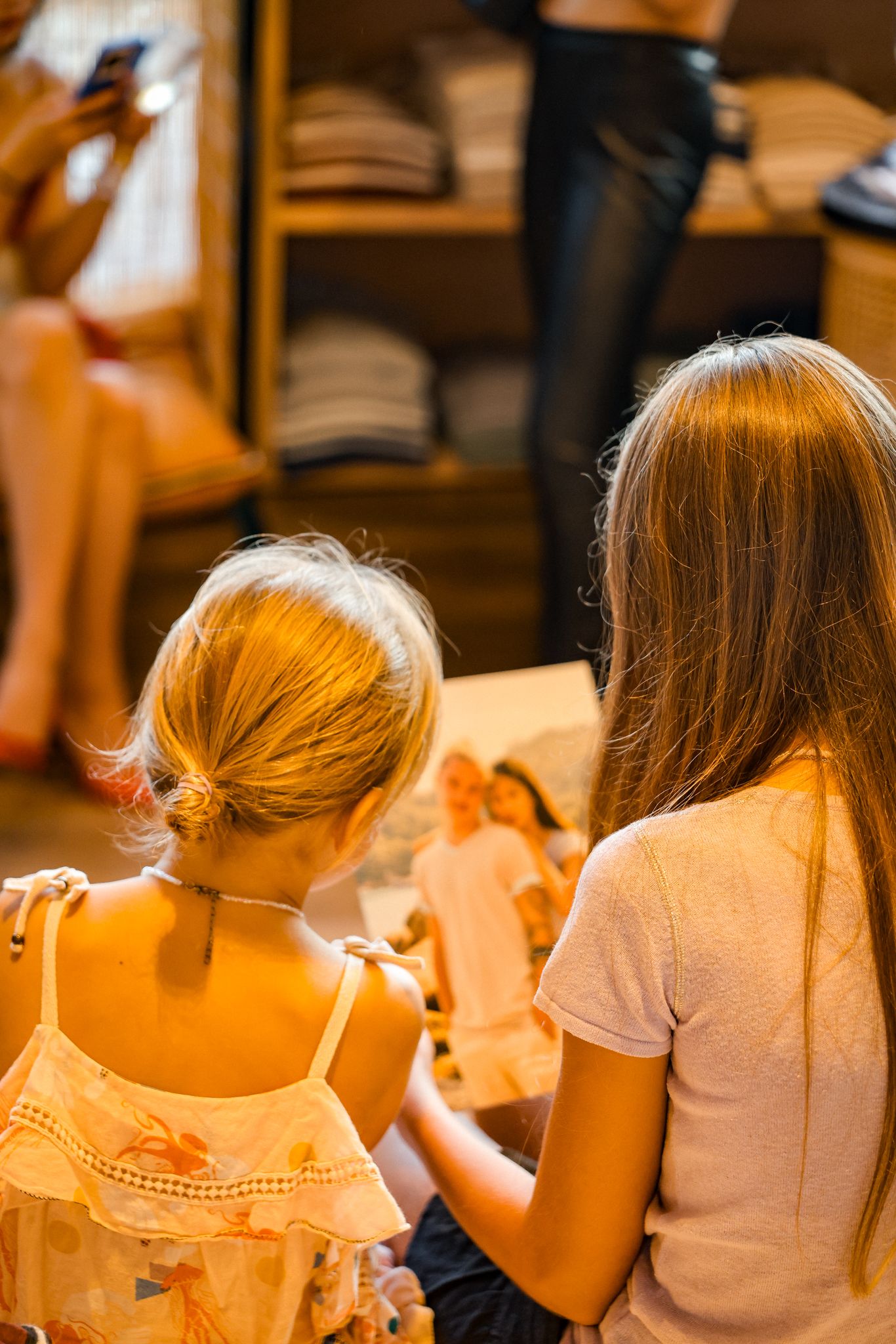 Two young girls with their backs turned browsing items in a warmly lit retail clothing store.