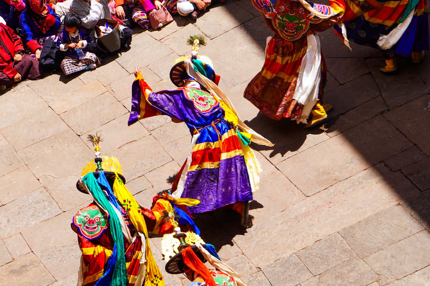 Colorfully costumed performers in ornate masks dance at a traditional Bhutanese Tsechu festival.