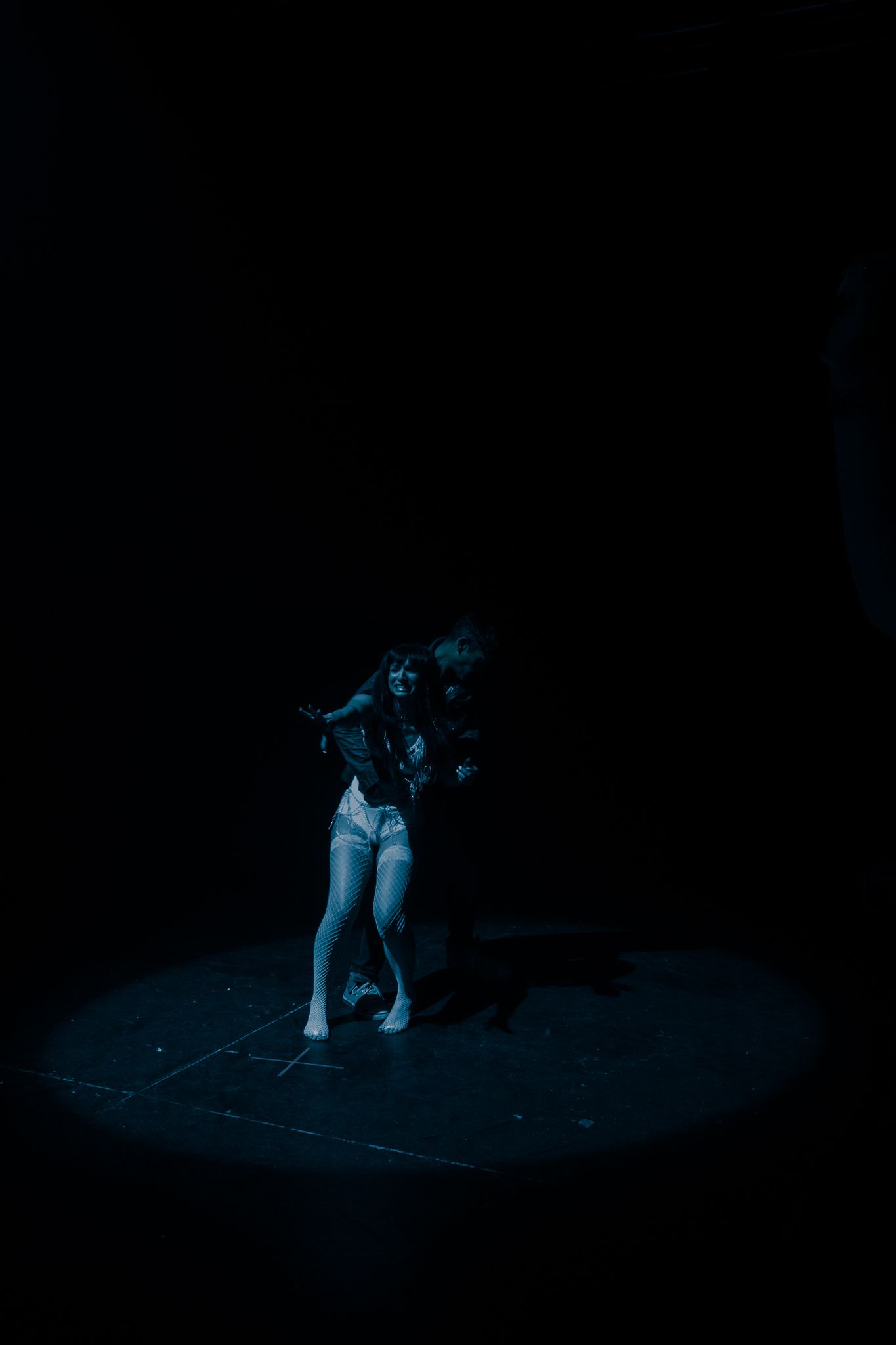 A female dancer performs energetically under a blue spotlight on a dark stage.