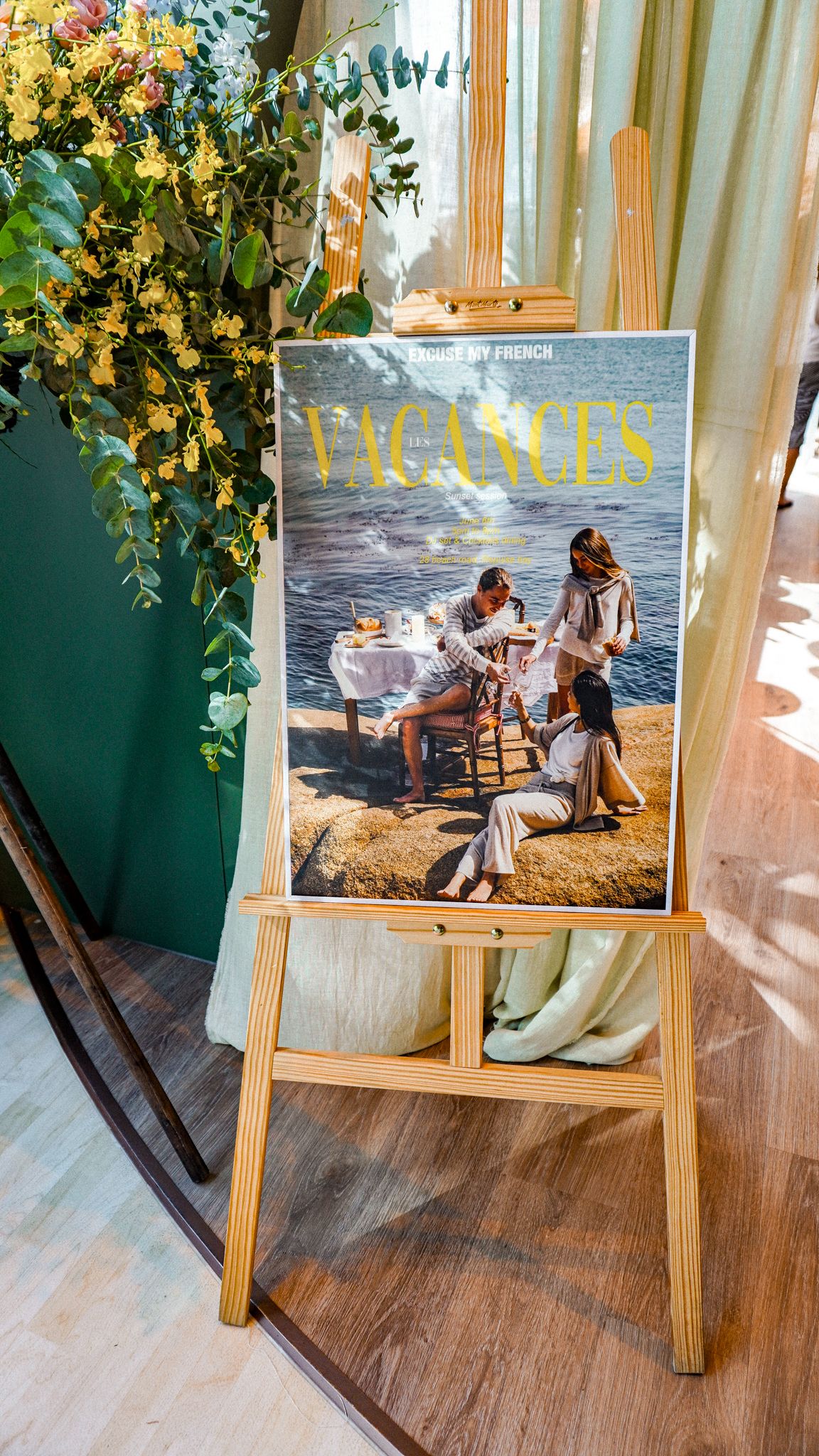 A Vacances magazine cover displayed on a wooden easel surrounded by yellow flowers.