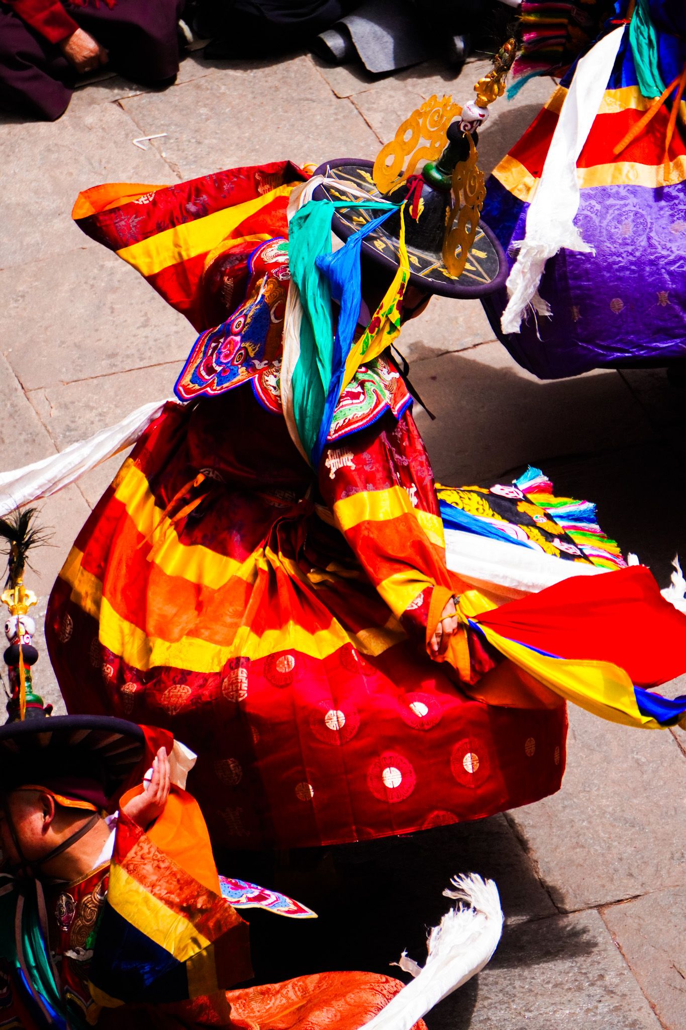 Colorful Tibetan Cham mask dancer in vibrant red and yellow robes performing traditional Buddhist festival dance.