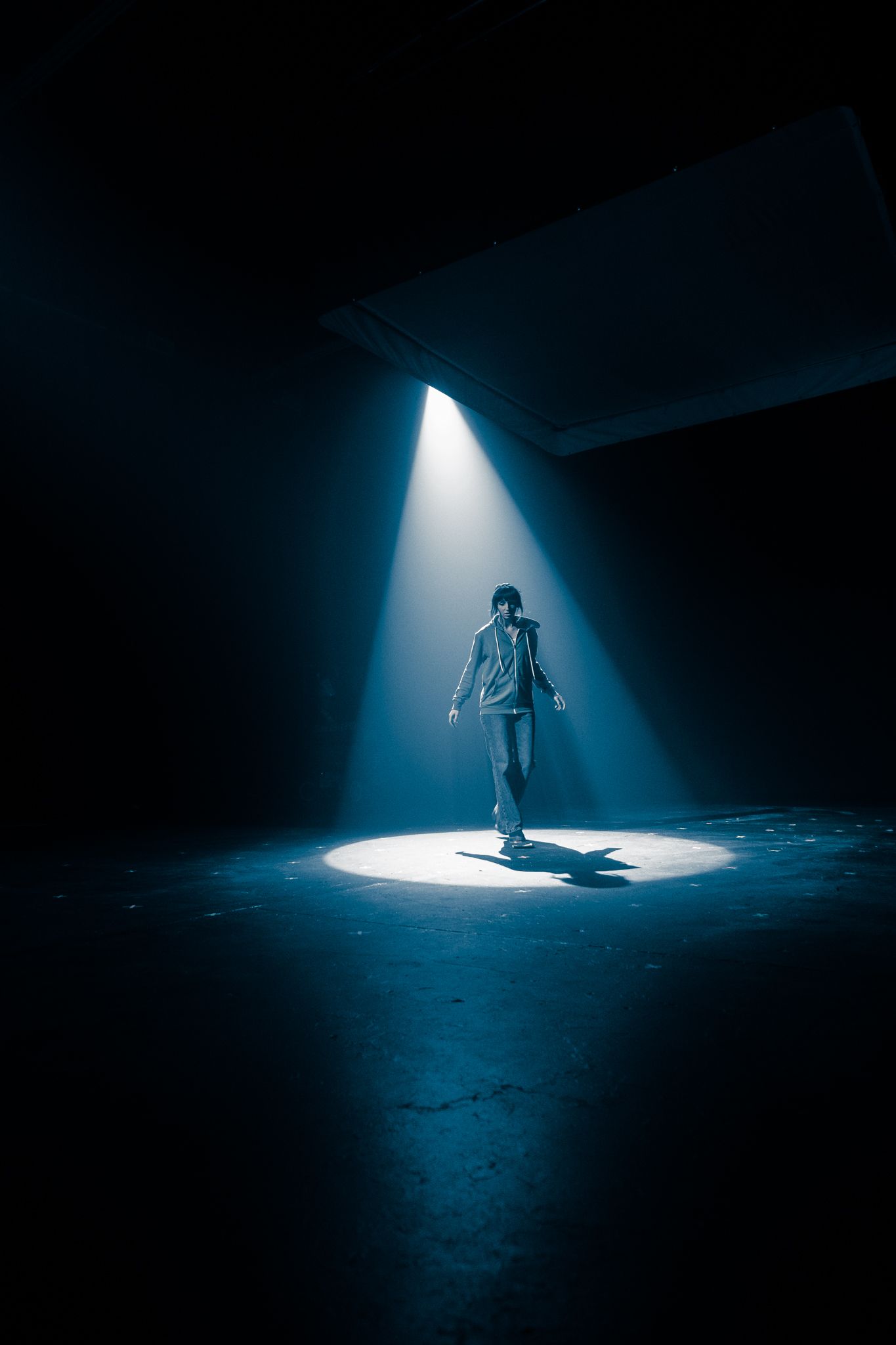 Person walking through an intense blue spotlight beam in a dark atmospheric studio space.