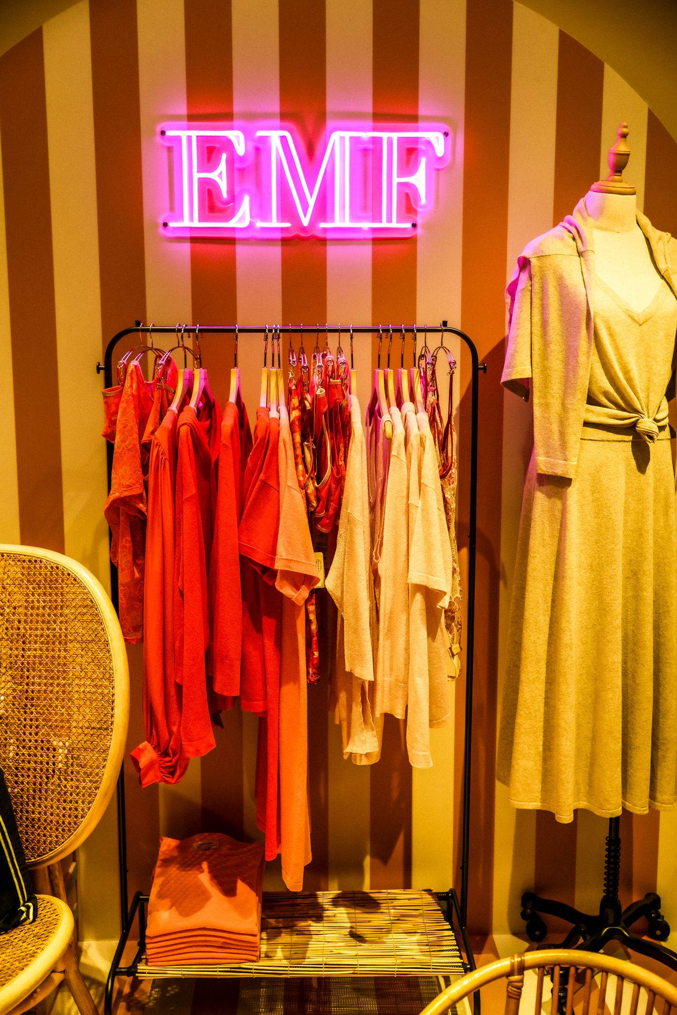 A clothing rack with red and neutral garments under a pink EMF neon sign.