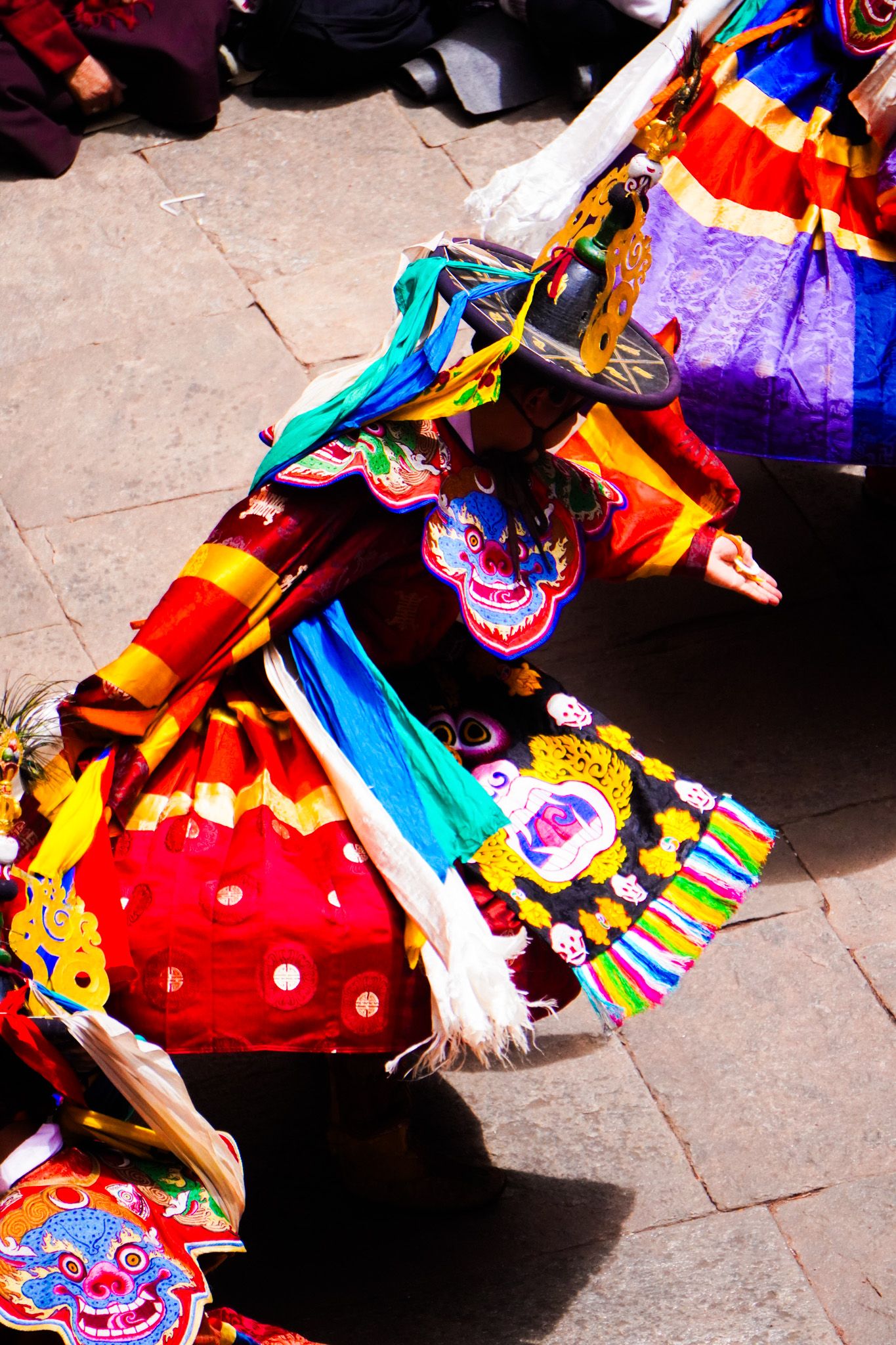 Two Tibetan Cham dancers in colorful costumes and elaborate masks performing traditional Buddhist festival dance.