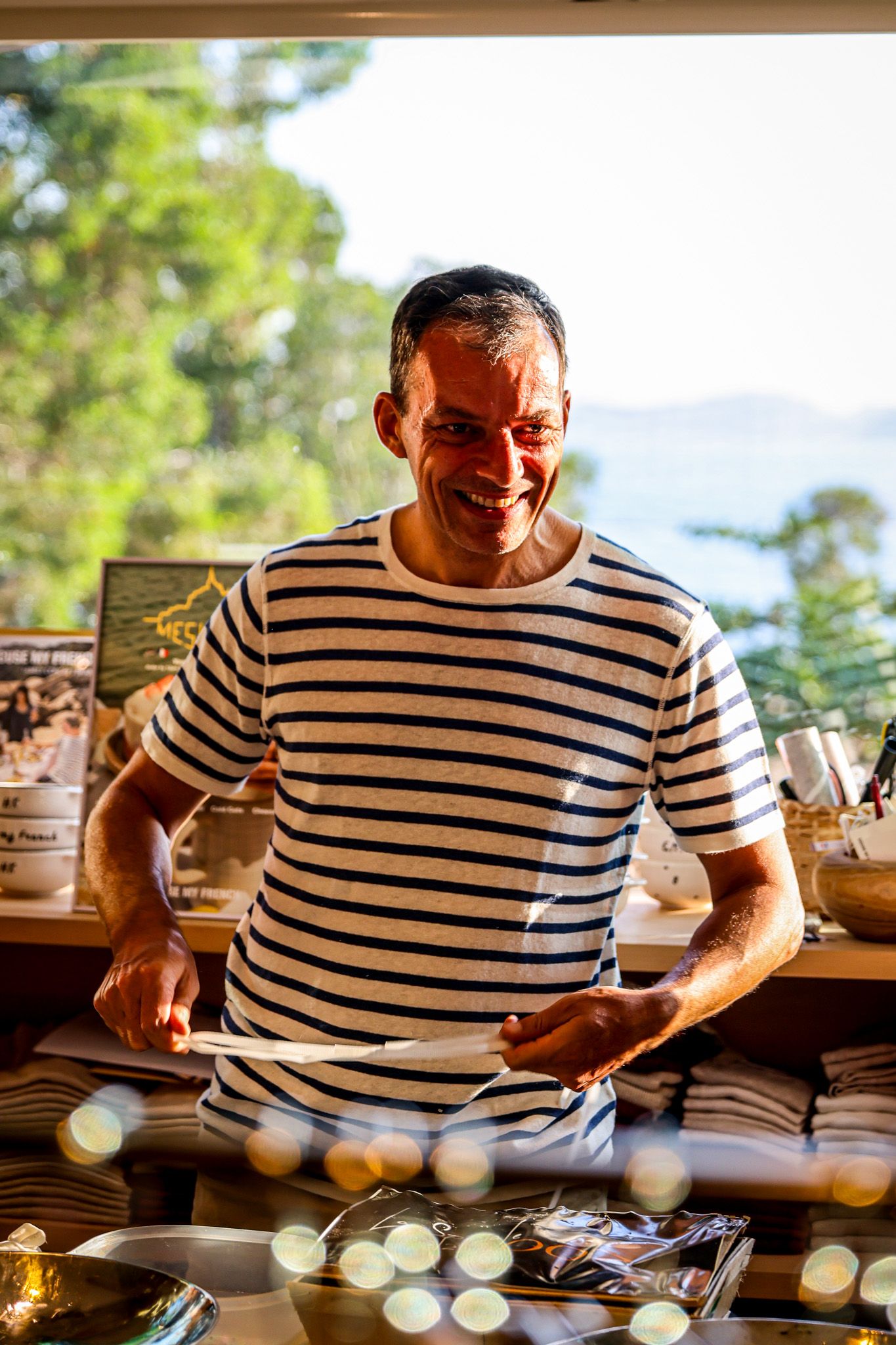 A smiling man in a striped shirt folds clothing at a retail store counter.