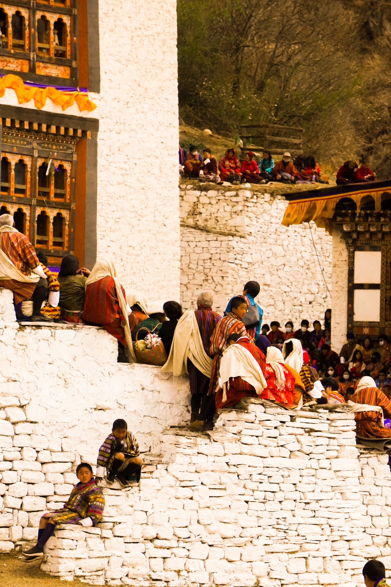 Crowds gather on white stone steps of a traditional Bhutanese dzong during a religious festival.