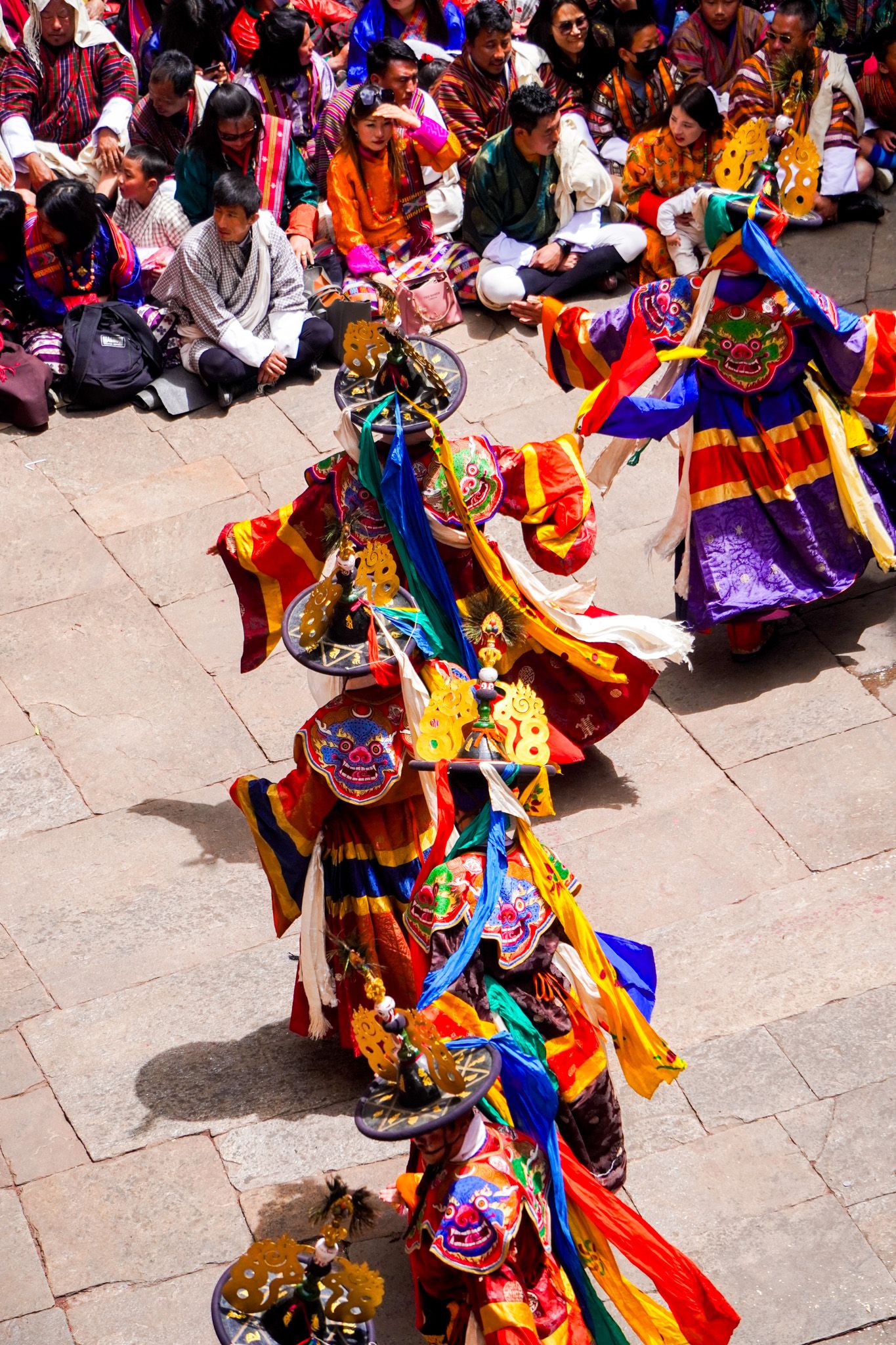 Overhead view of vibrant Tibetan Cham dancers in ornate masks and costumes at Buddhist festival.