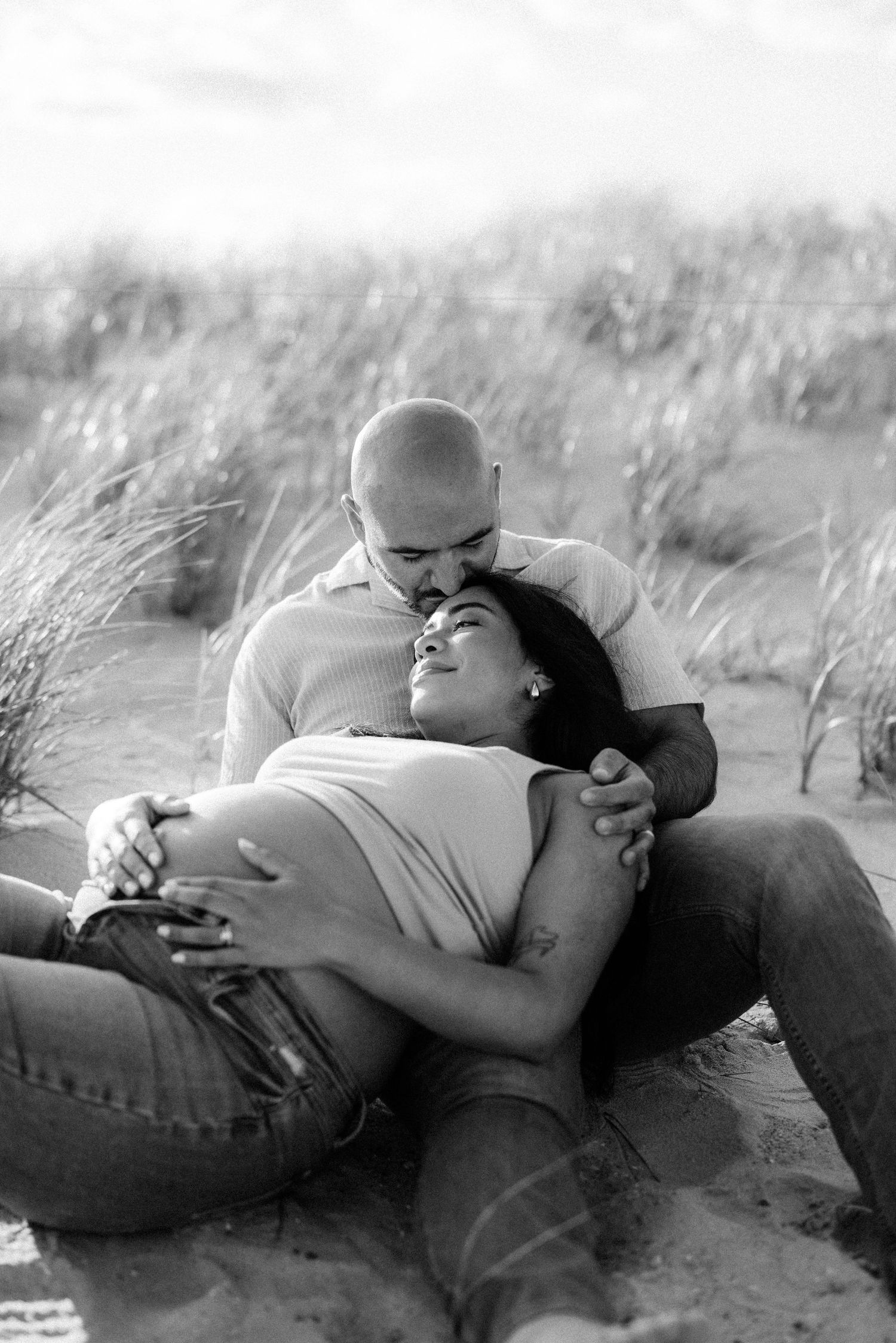 Black and white photo of a couple embracing tenderly on sandy dunes.