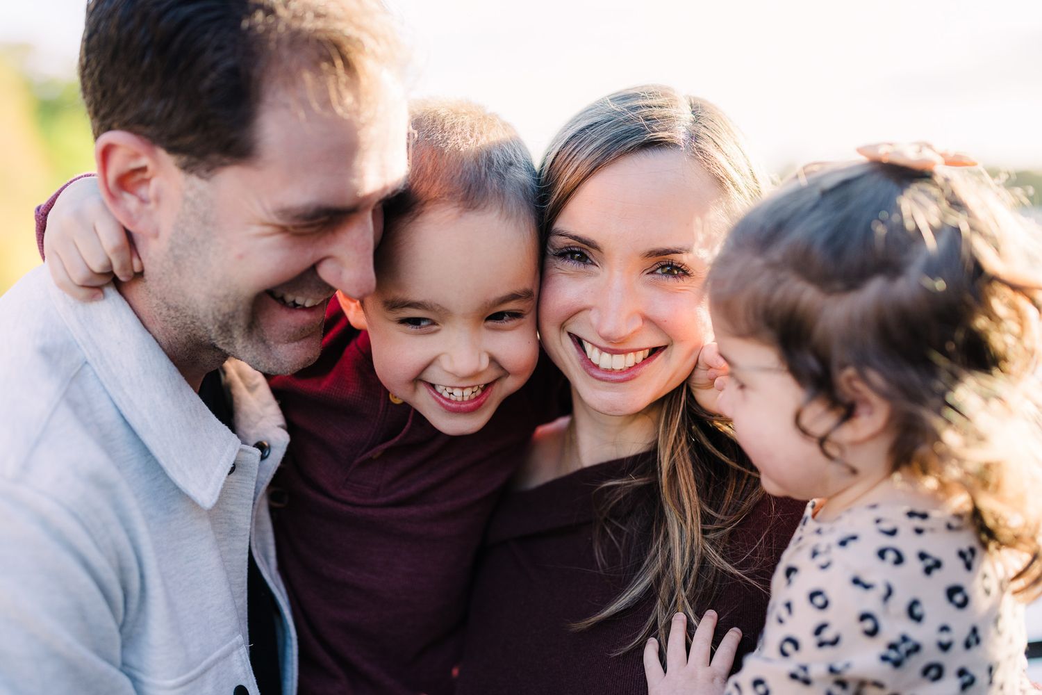 Happy family of four sharing a warm embrace outdoors, with two young children smiling joyfully with their parents.