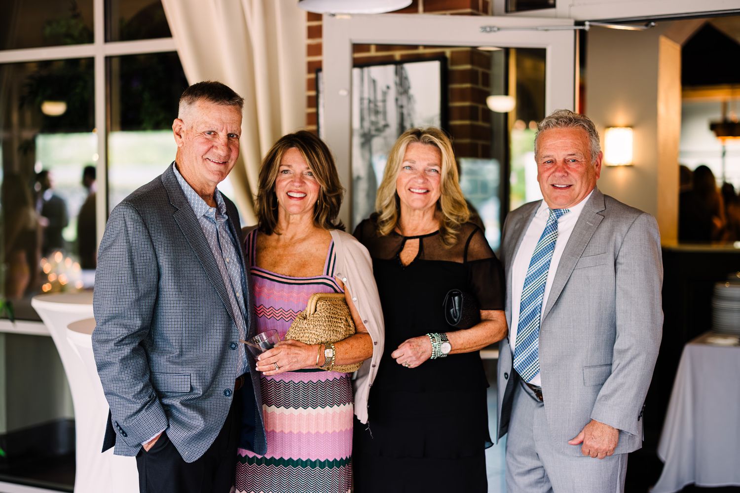 Four adults smiling together at an elegant indoor event, dressed in smart casual attire including blazers and a striped dress.