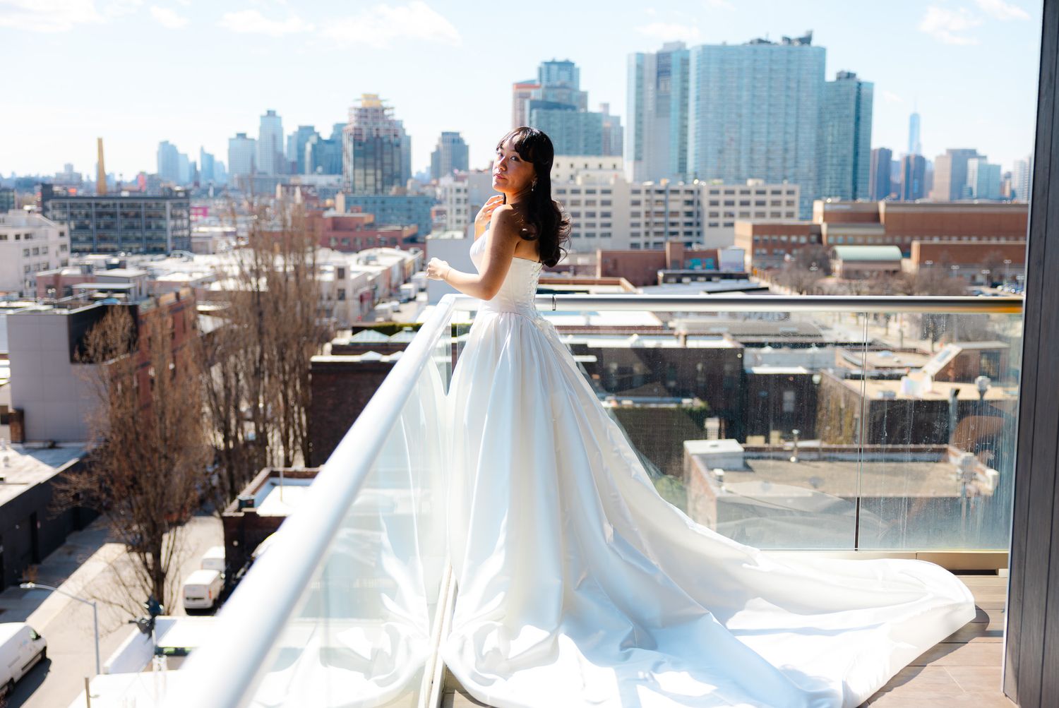 Bride in a stunning white ballgown posing on a rooftop balcony with city skyline views.