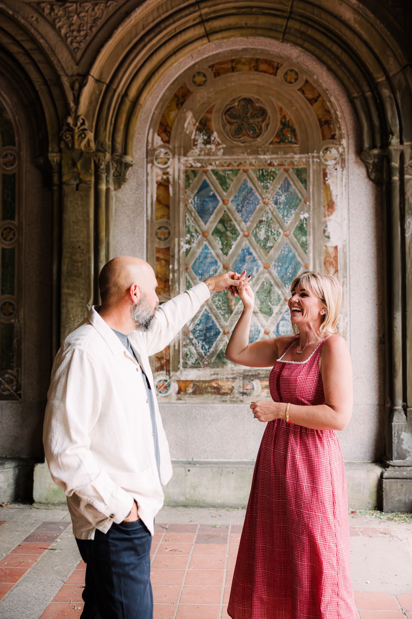 A couple dances joyfully under ornate arched architecture with colorful mosaic tiles in the background.