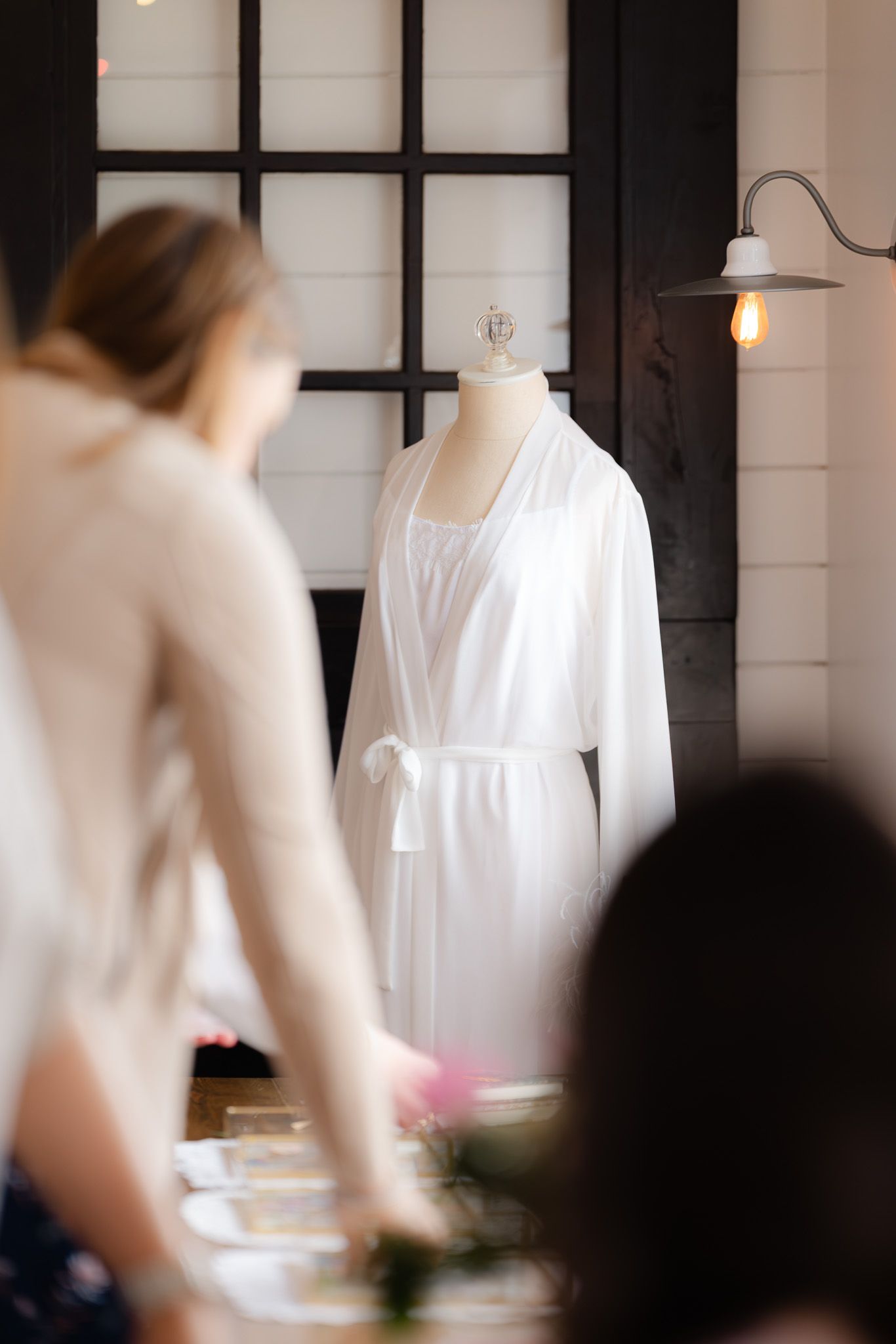 White silk bridal robe displayed on a mannequin in an elegant bridal suite with black window frames.