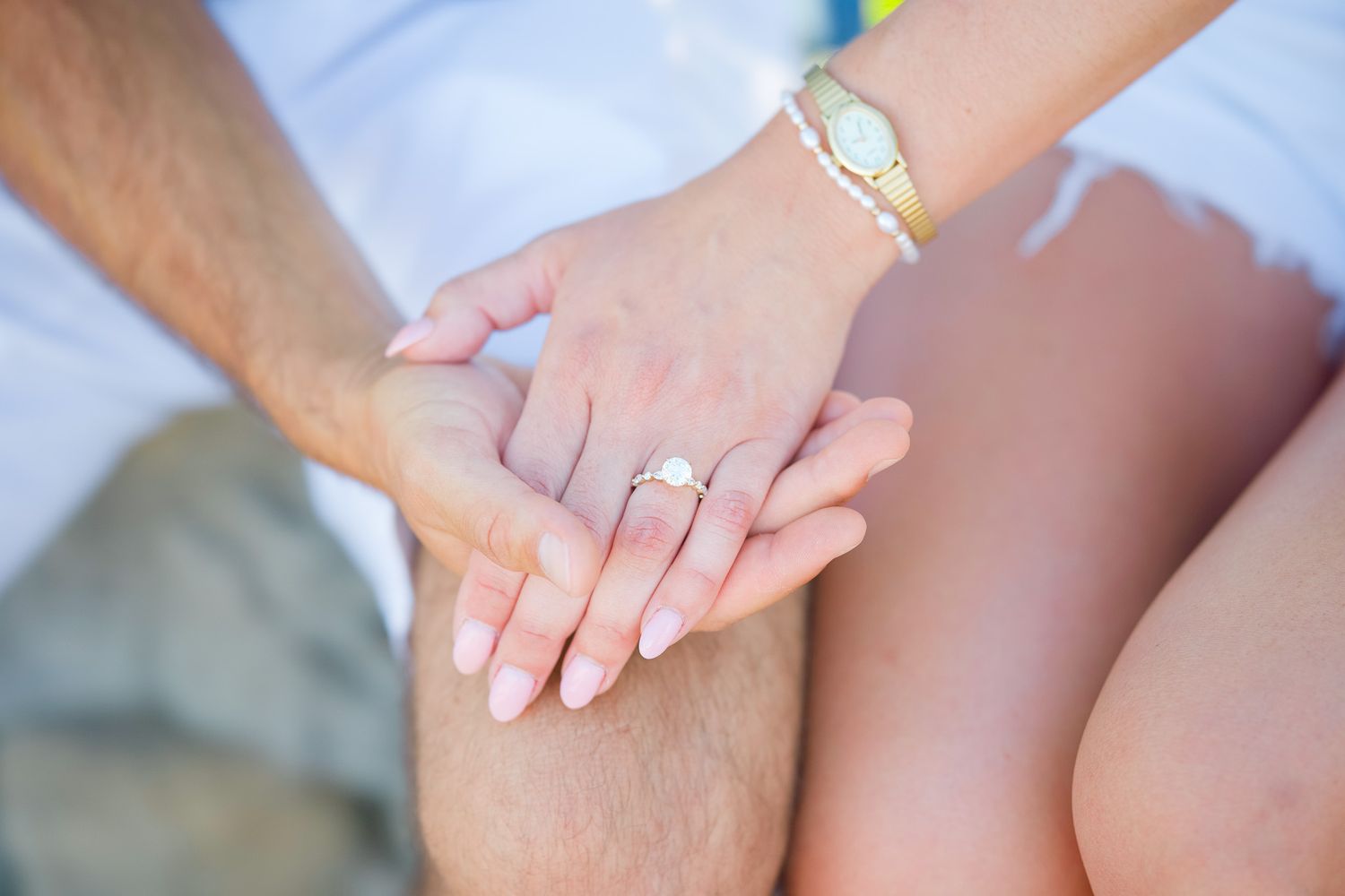 Close-up of a couple holding hands showing an engagement ring with diamond solitaire, woman wearing a gold bracelet and watch.