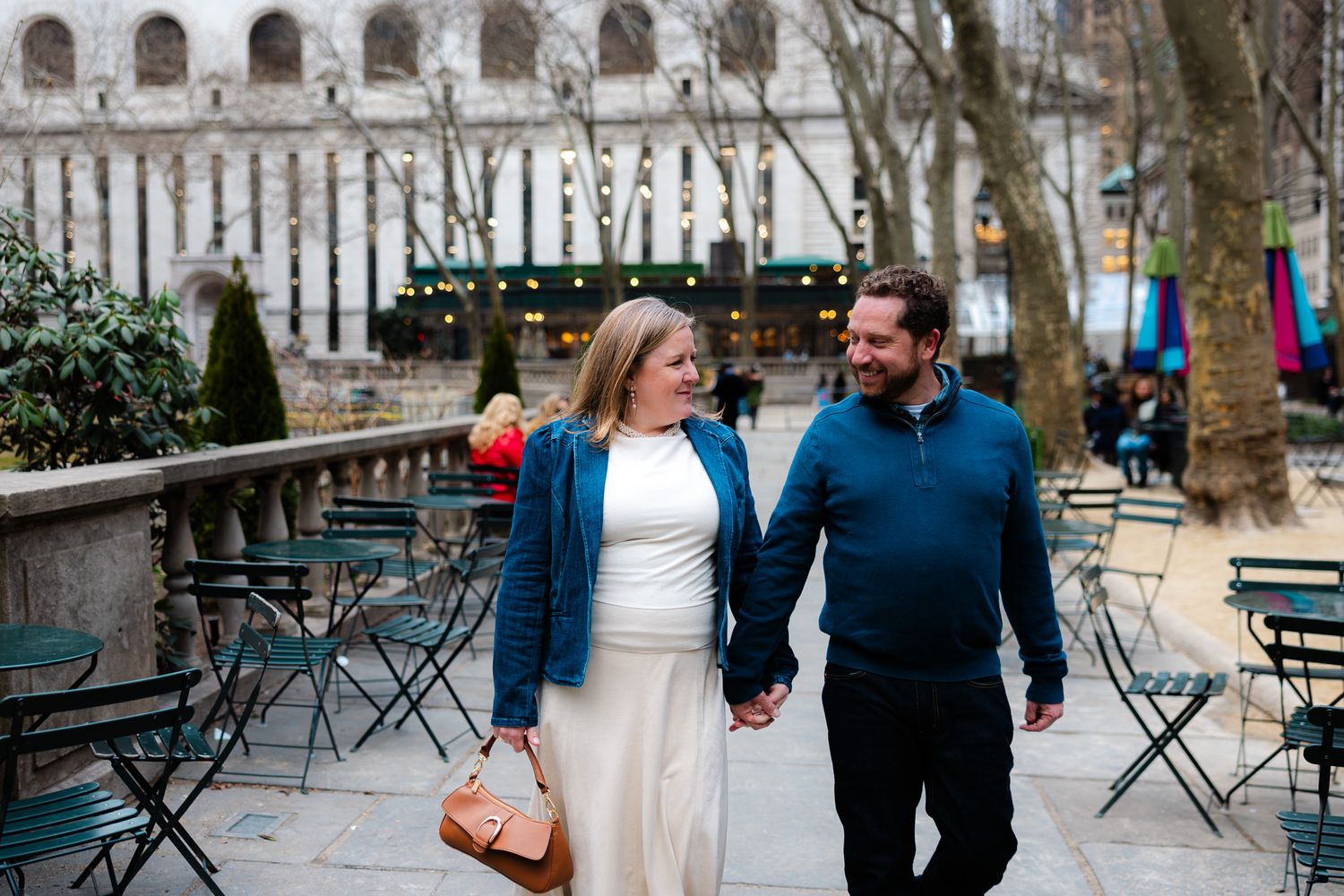 A couple holds hands and smiles while strolling through Bryant Park in New York City on a winter day.
