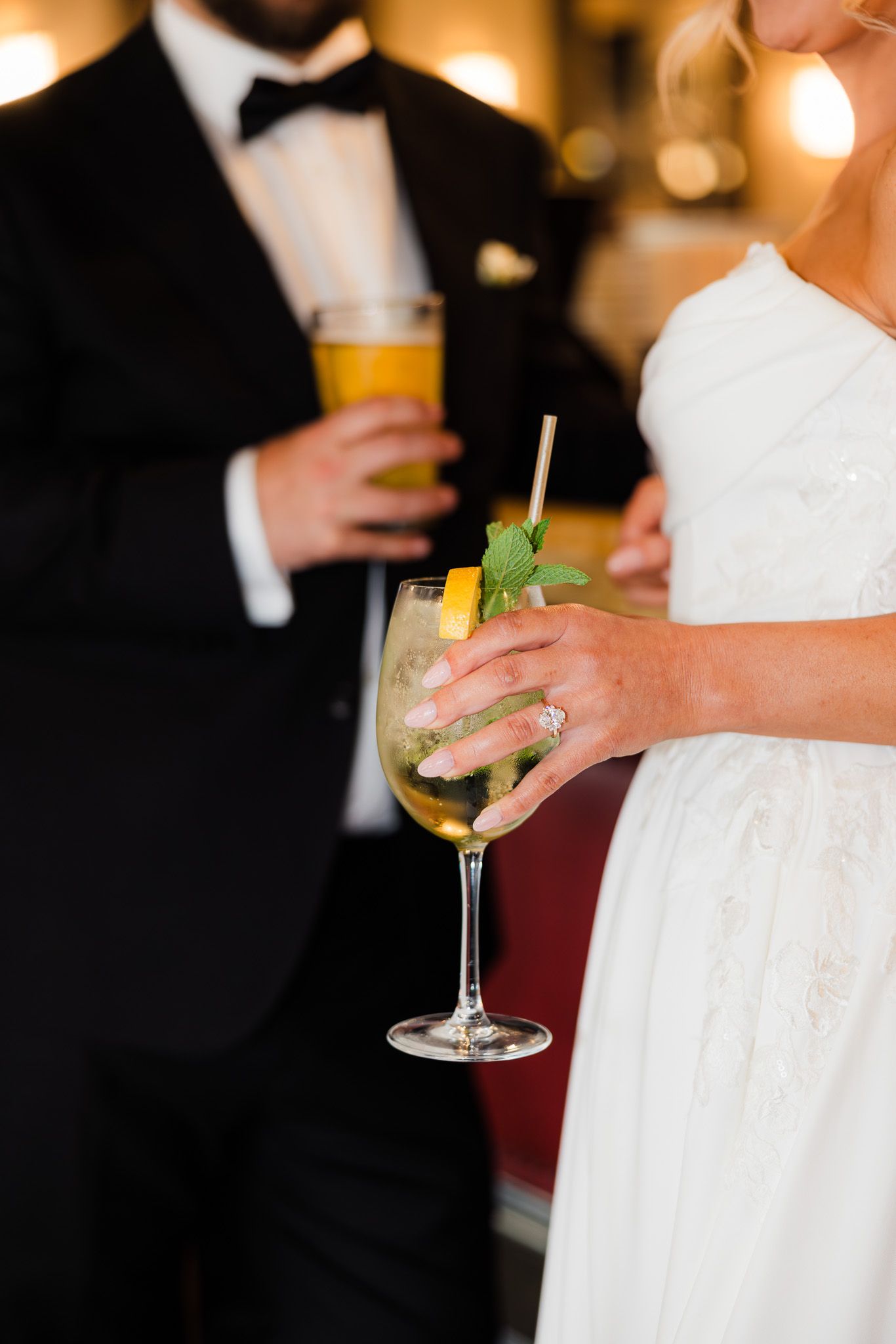 Bride in white dress and groom in tuxedo holding cocktails at wedding reception.
