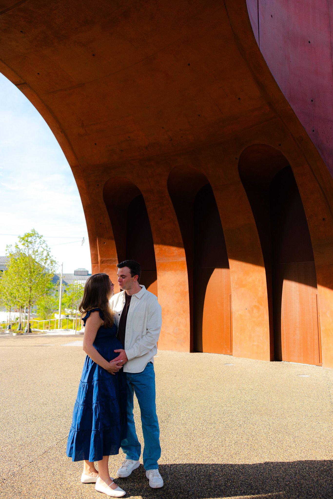 Couple sharing a romantic moment under a curved red architectural structure on a sunny day.