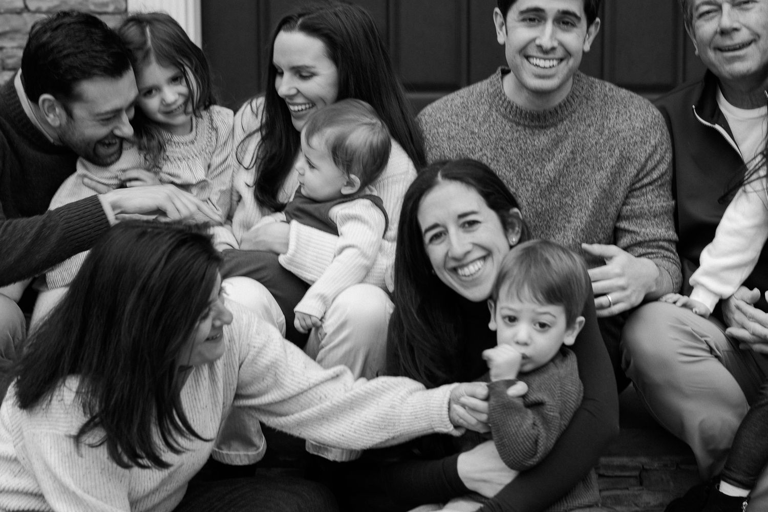 Black and white family portrait of multi-generational group smiling together outdoors, including children and babies.
