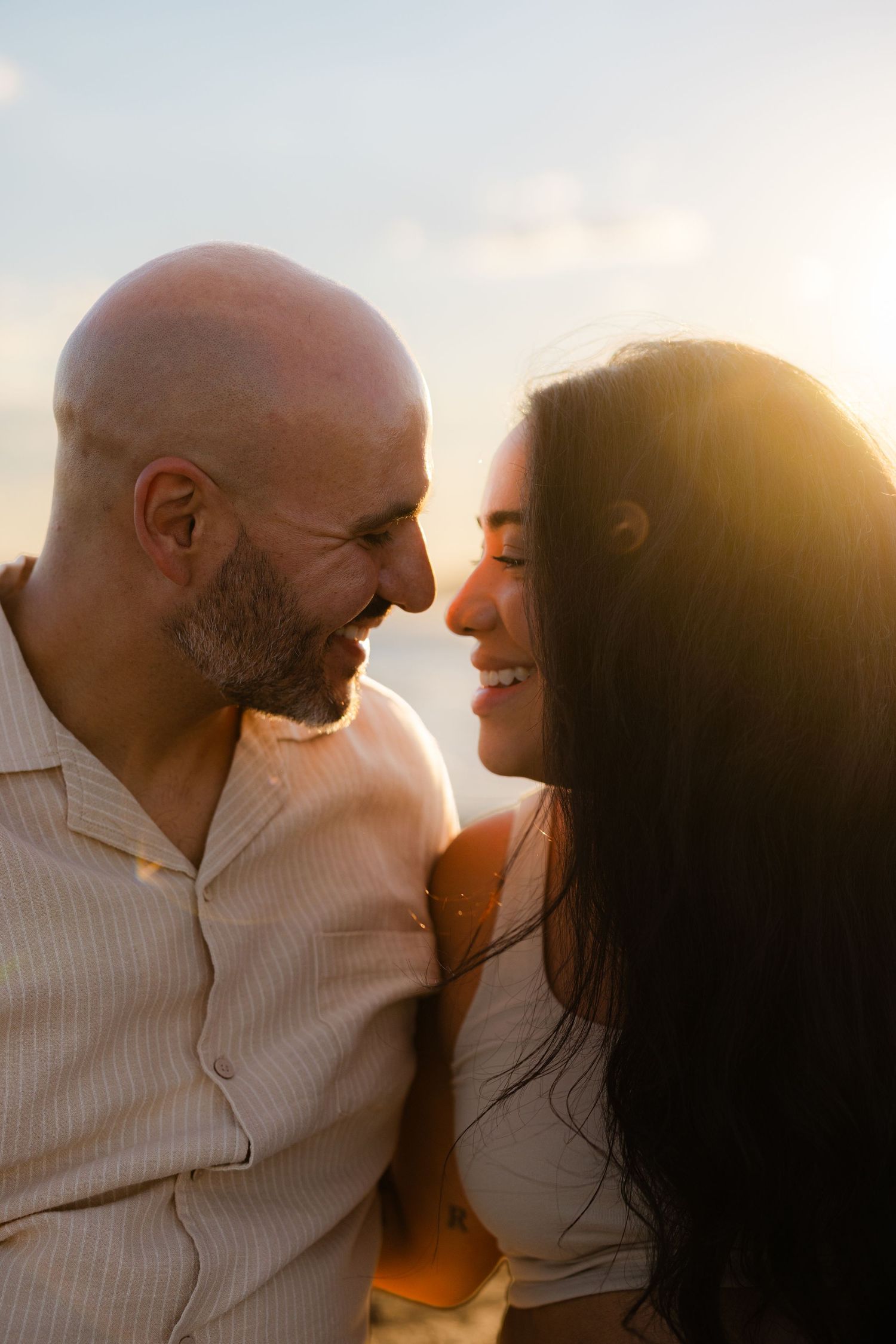 Couple smiling and gazing at each other during a golden sunset outdoors.