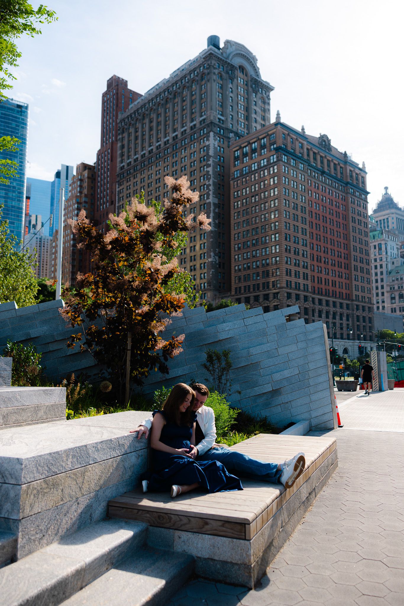 Couple sitting together on stone steps in an urban park with a large brick skyscraper in the background.