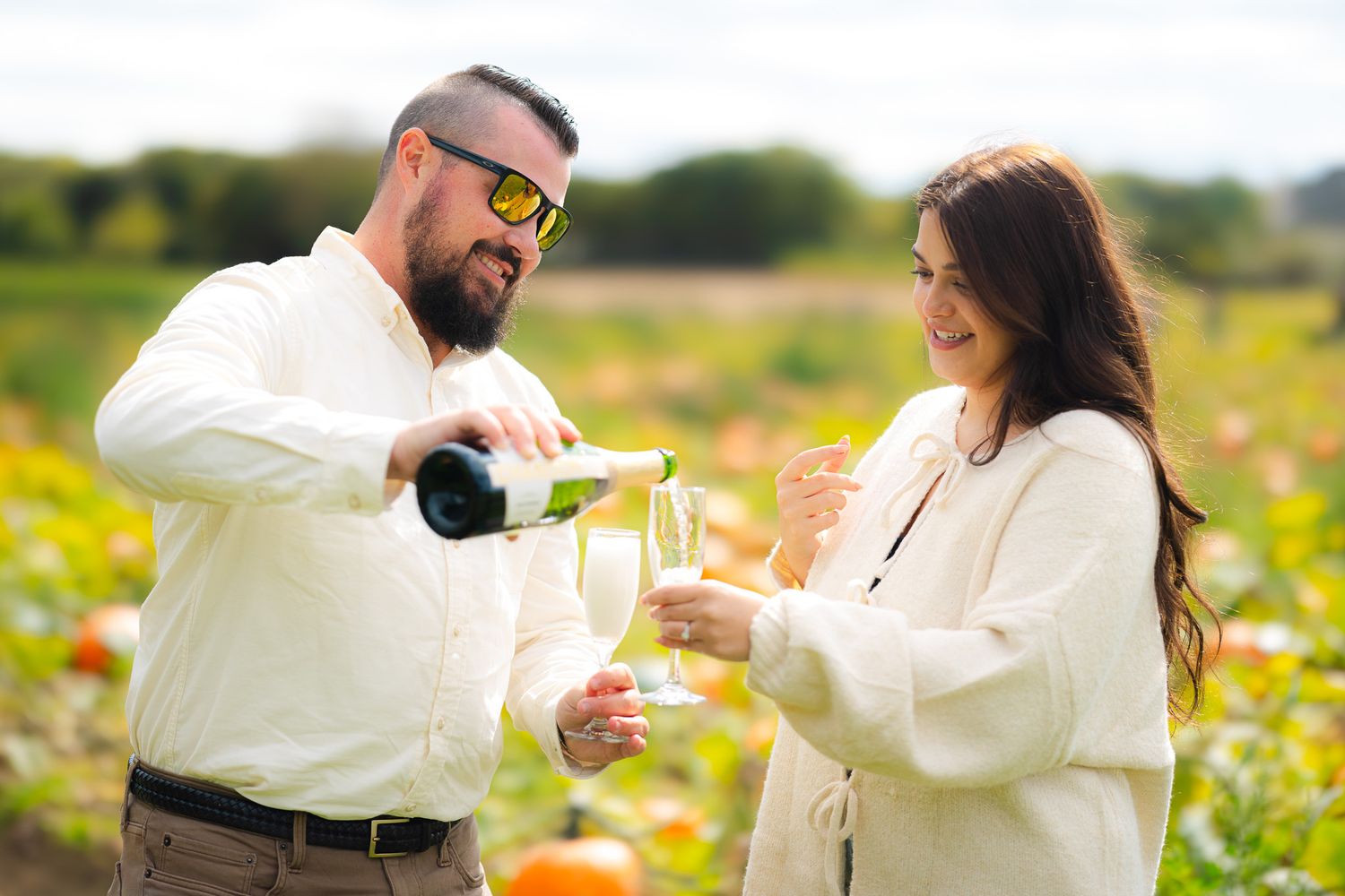 Happy couple pouring champagne to celebrate engagement in an outdoor pumpkin field.