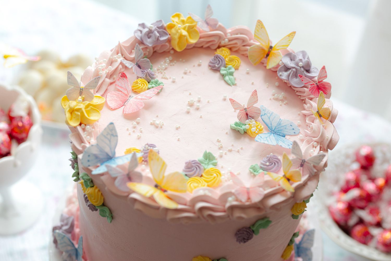 Pink birthday cake decorated with pastel butterfly and flower fondant toppers on a white dessert table.