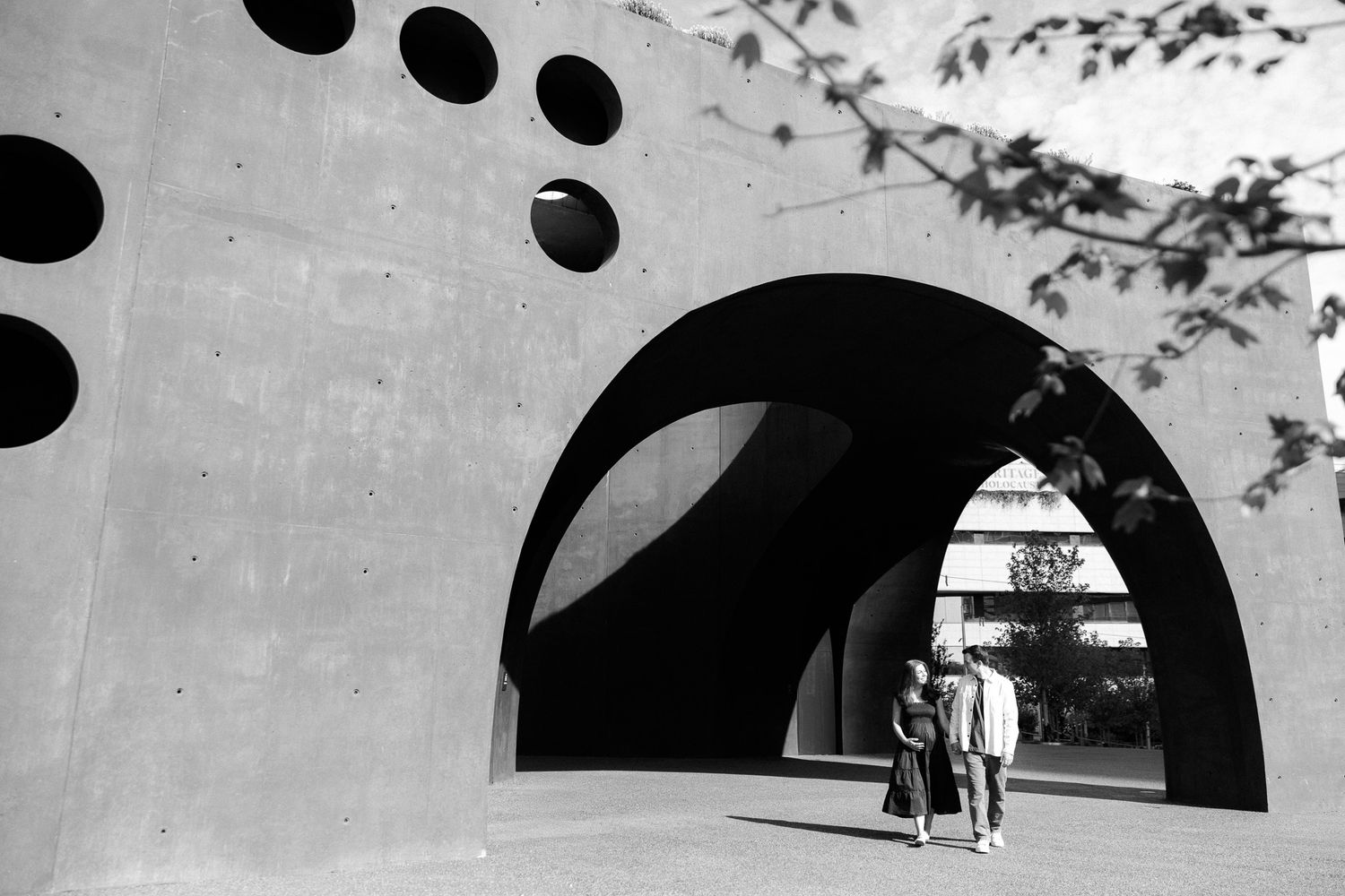 Couple walking through a modern concrete architectural structure with circular cutouts in black and white photography.