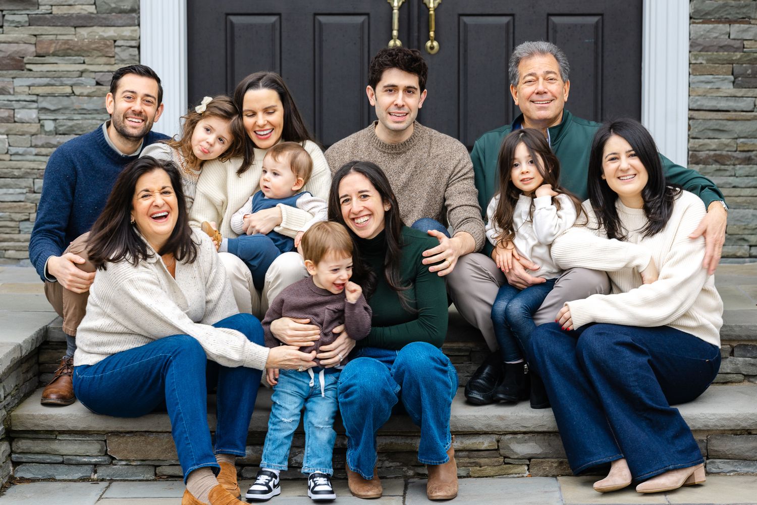 Large multigenerational family smiling together on stone steps outside a home.
