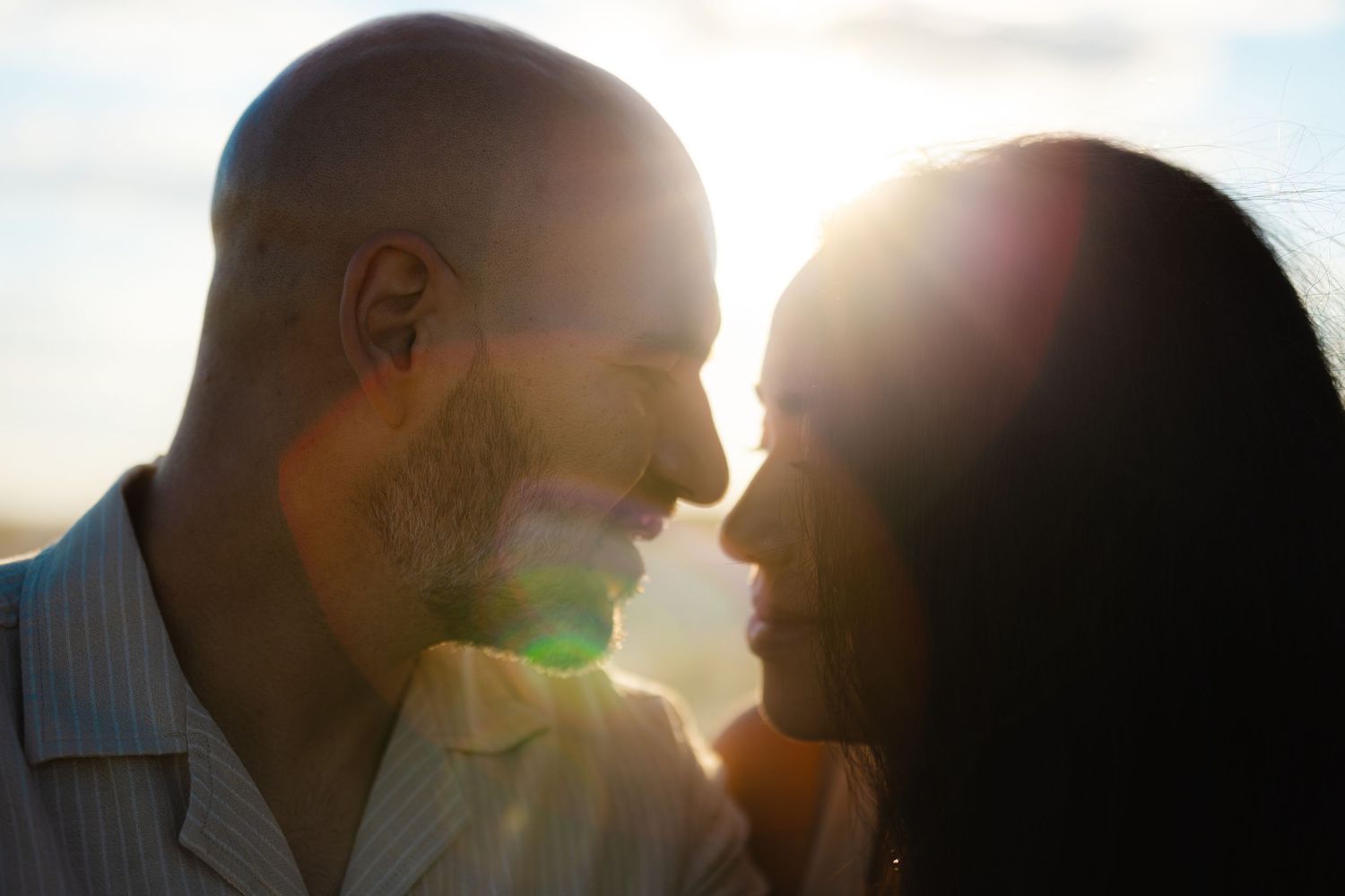 Romantic couple sharing a tender moment at sunset with golden lens flare glowing between them.
