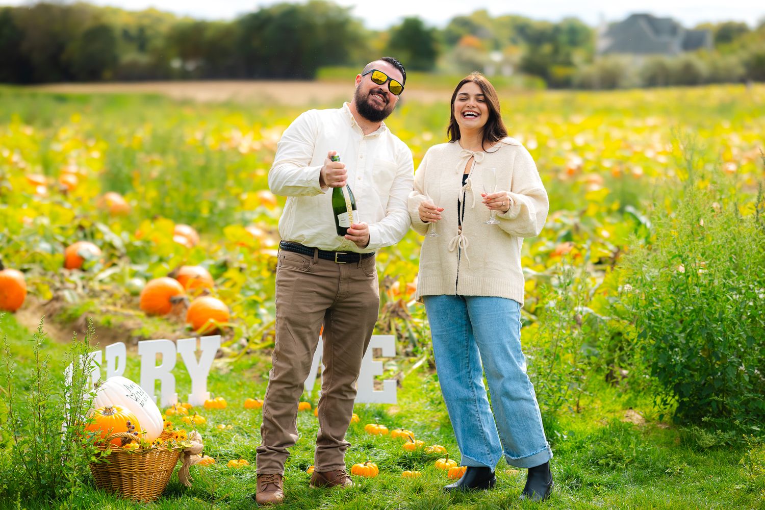 Engaged couple celebrating with champagne in a sunny pumpkin patch after proposal.