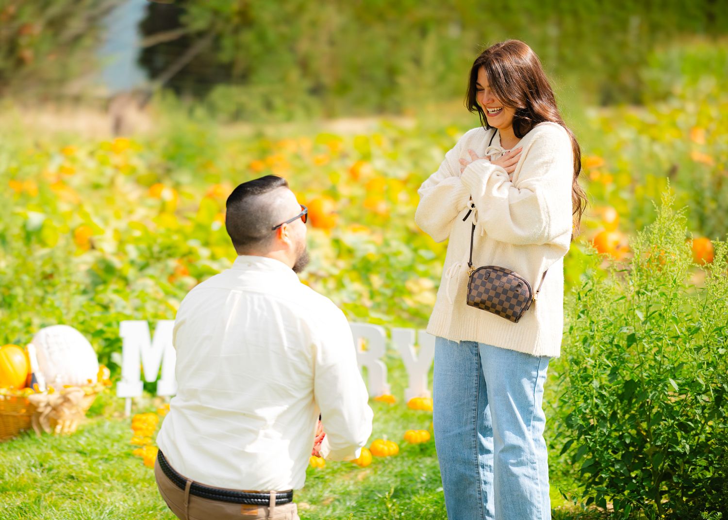 Man on one knee proposing to woman in a colorful pumpkin patch field.