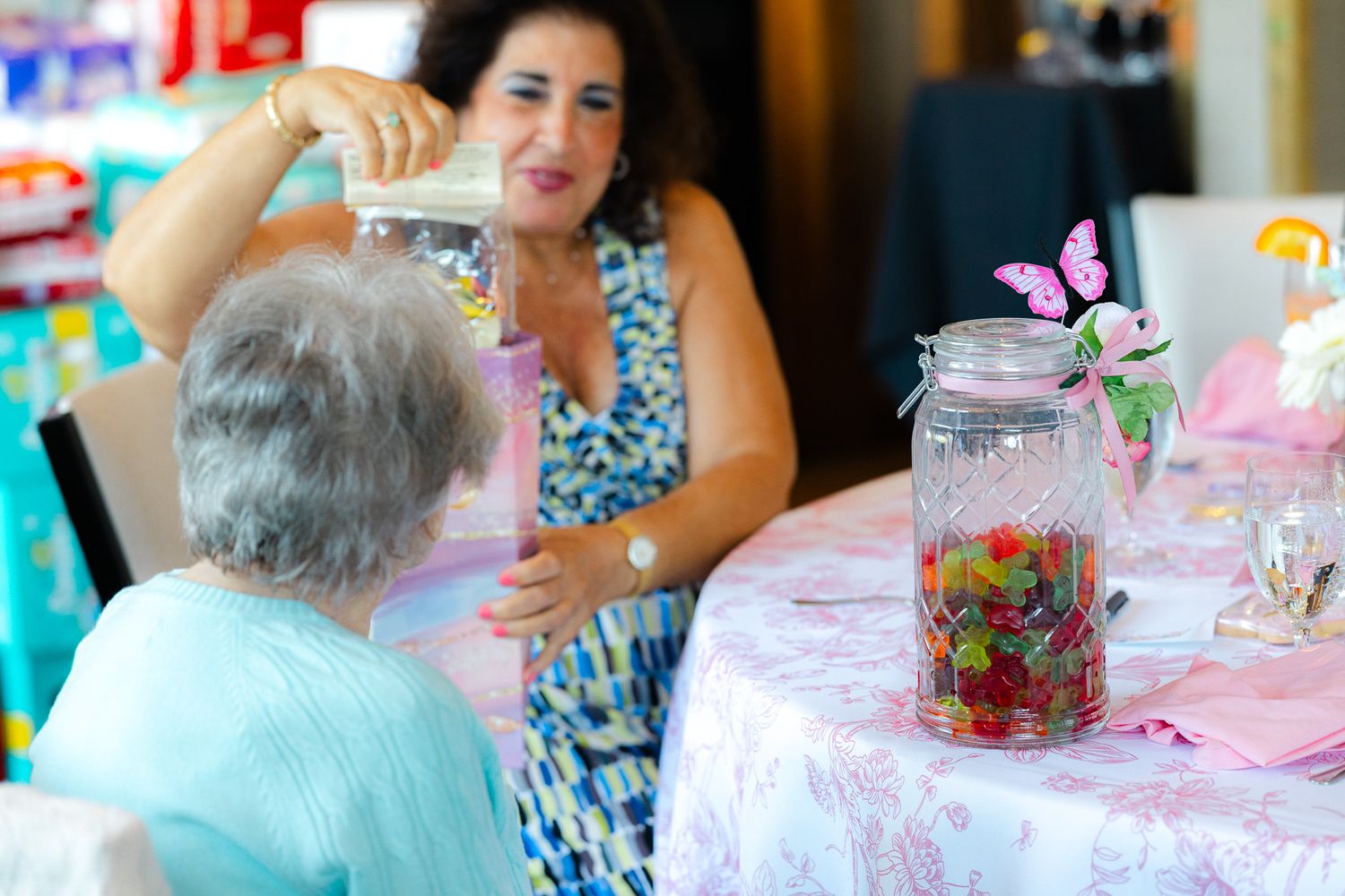 Two women at a decorated table with a candy jar and butterfly ornament at a festive party event.