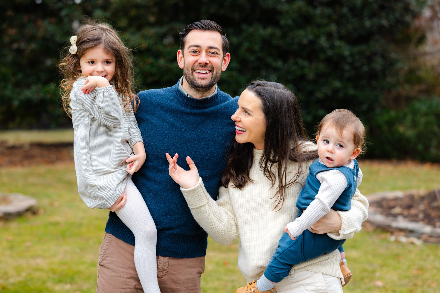 Happy couple holding two young children outdoors in a green backyard setting.