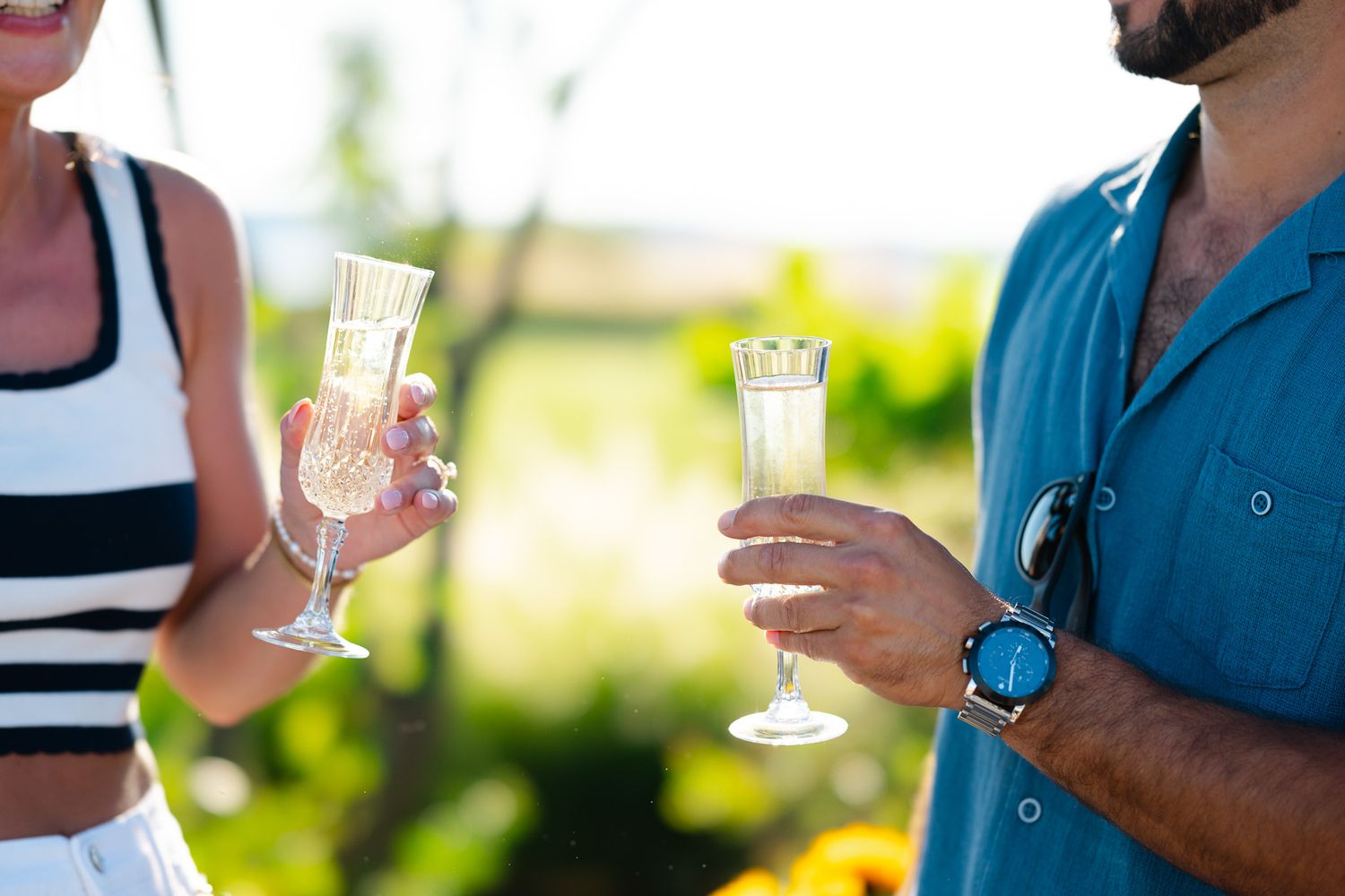Couple celebrating outdoors toasting with champagne flutes in a sunny garden setting, man wearing a smartwatch.